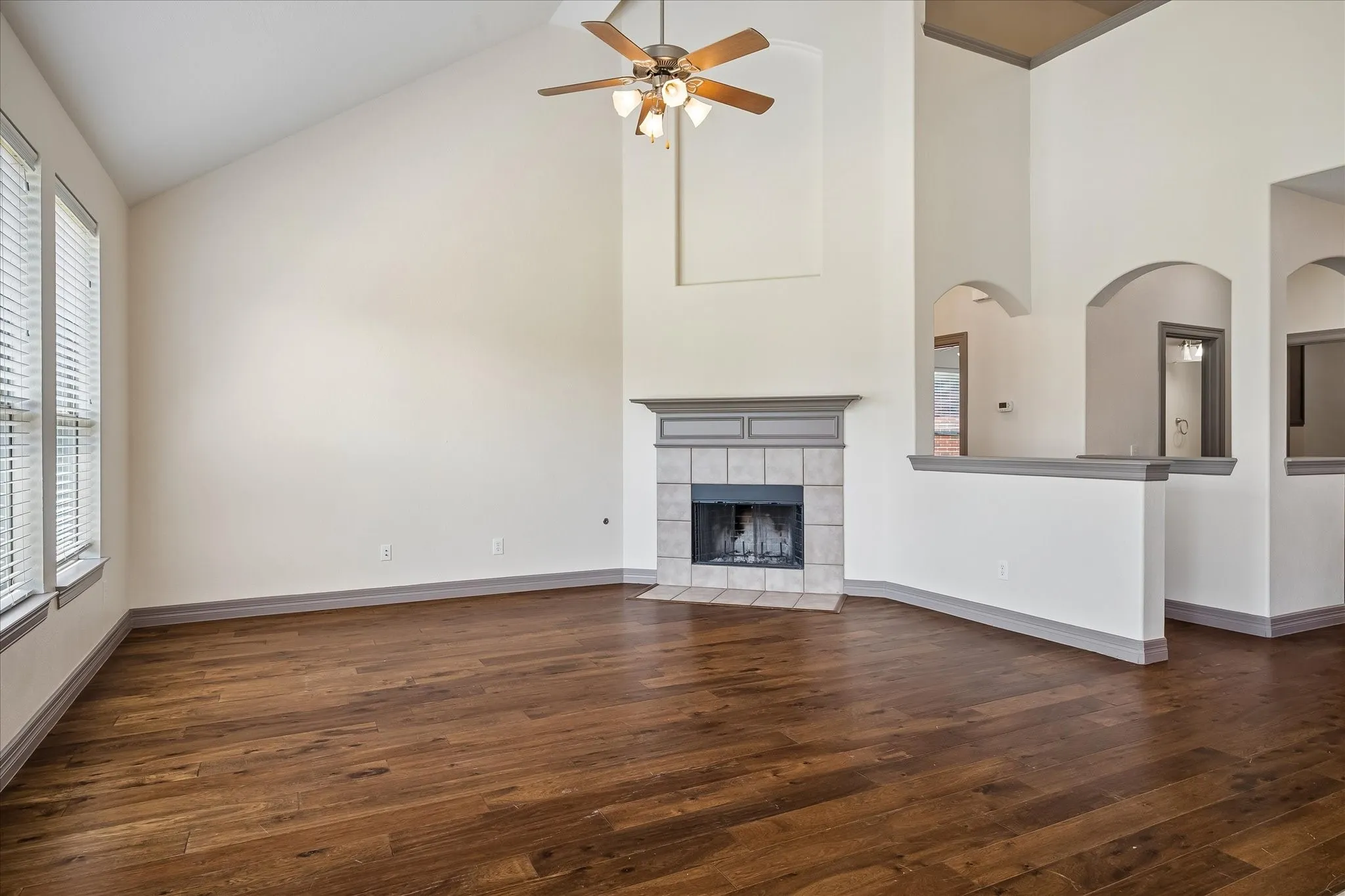 Vaulted ceiling with a ceiling fan, fireplace with a tile surround and mantel, wood-finish flooring, and arched doorways