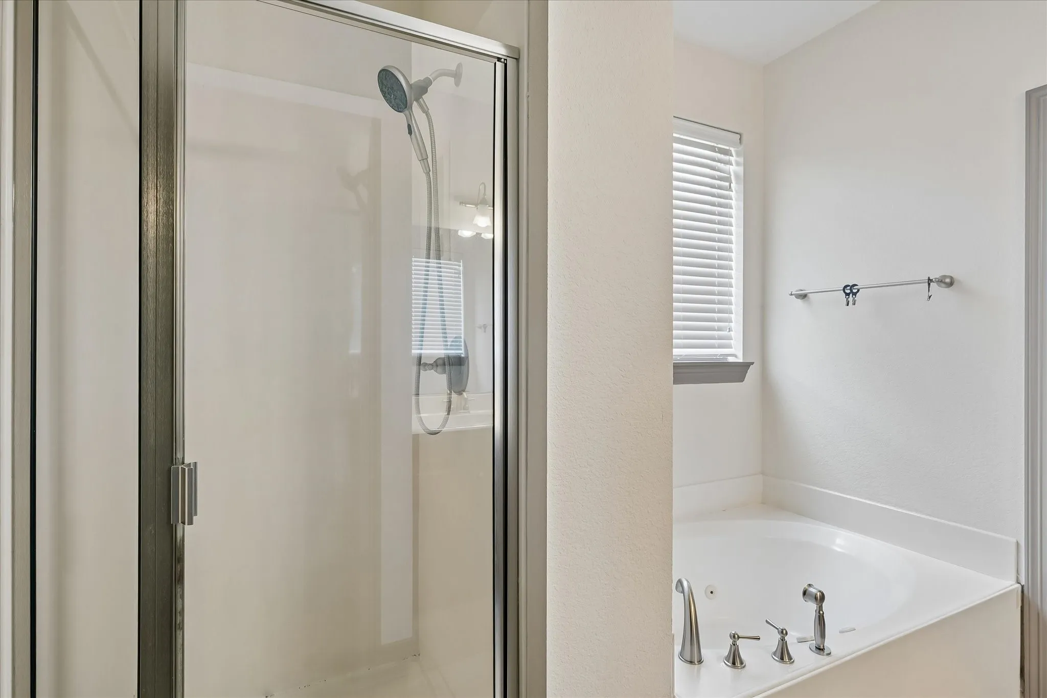Glass-enclosed shower, corner soaking tub with deck-mounted brushed nickel fixtures, and a window with blinds