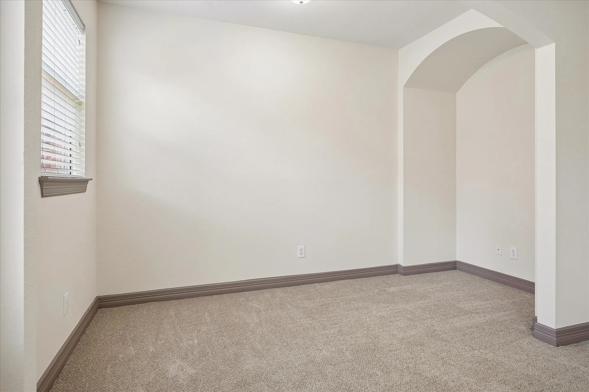 Arched entry, neutral carpeting, window with blinds, and white walls