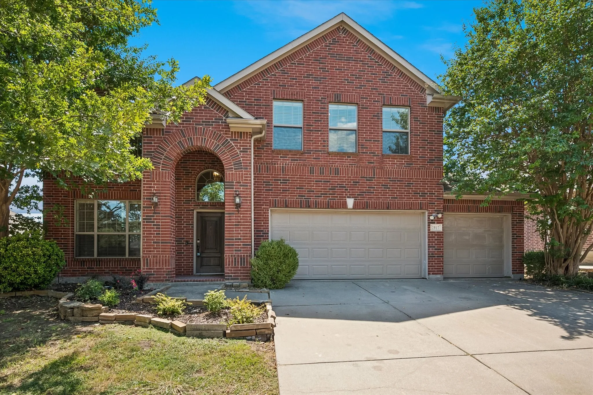 Brick exterior with a prominent arched entry, multiple windows, a two-car garage, an additional single-car garage, and landscaped planting beds