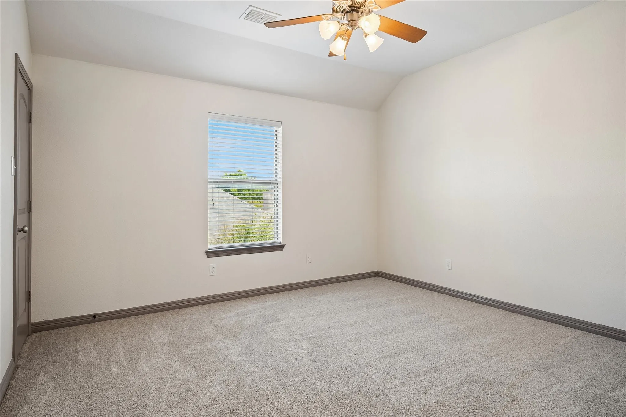 Neutral wall paint, carpet flooring, window with blinds, ceiling fan with light fixture, and a paneled door