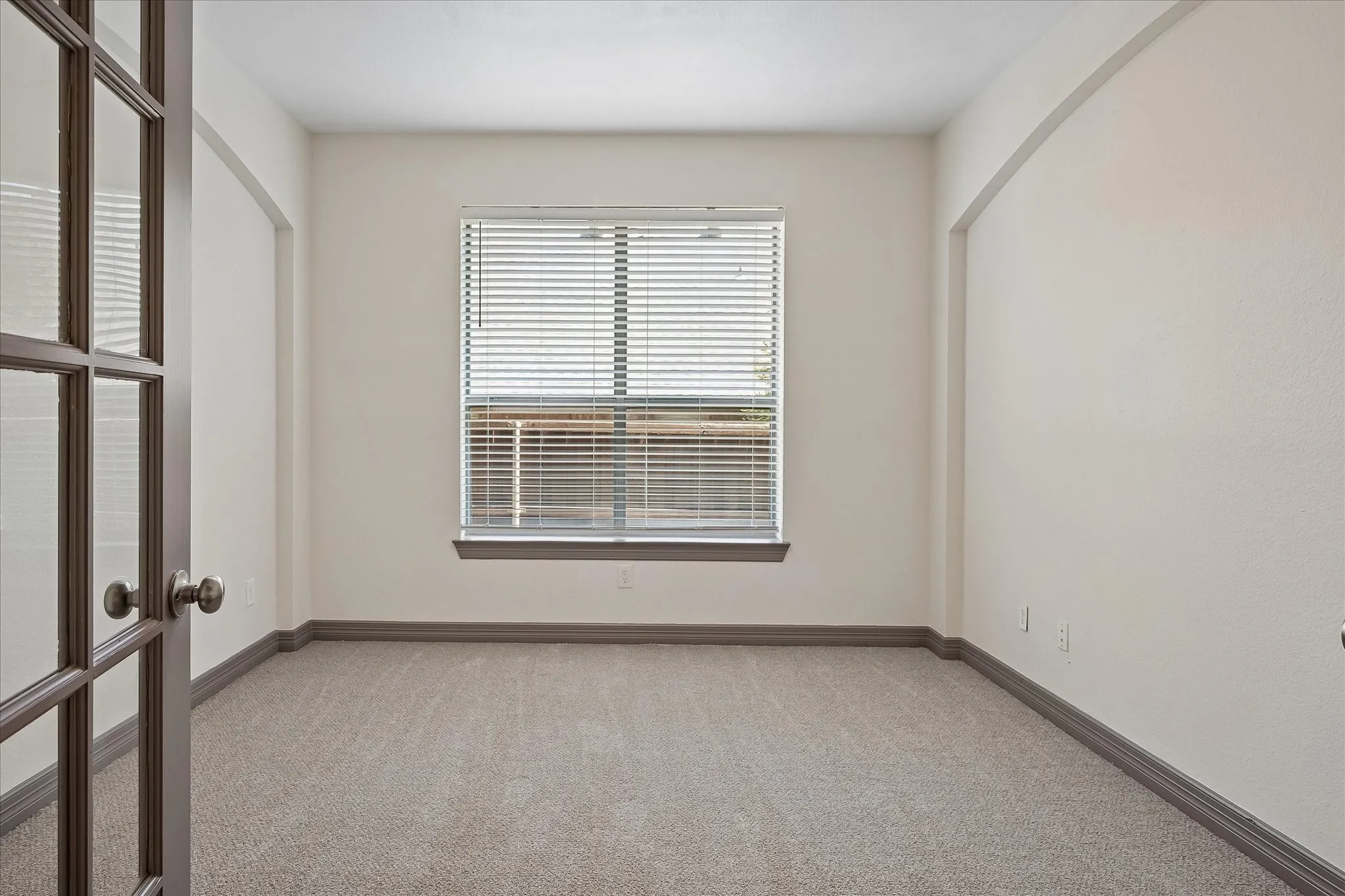 French doors with glass panes, single window with horizontal blinds, neutral wall paint, gray carpeting, and gray baseboards