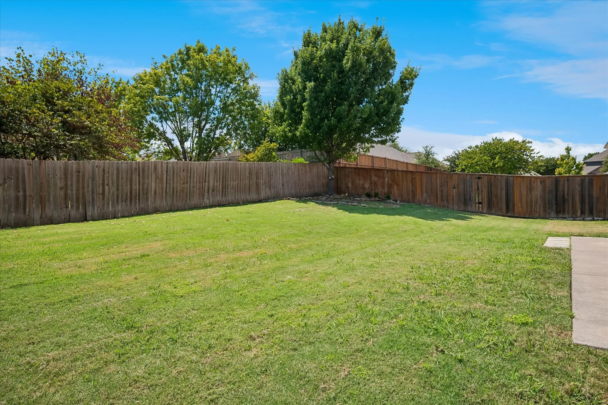 Expansive grassy yard with mature trees and perimeter wood fencing
