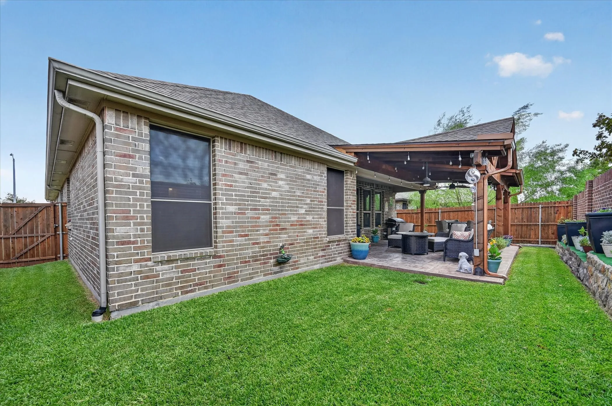 Brick exterior with a covered patio, wood pergola, and fenced yard
