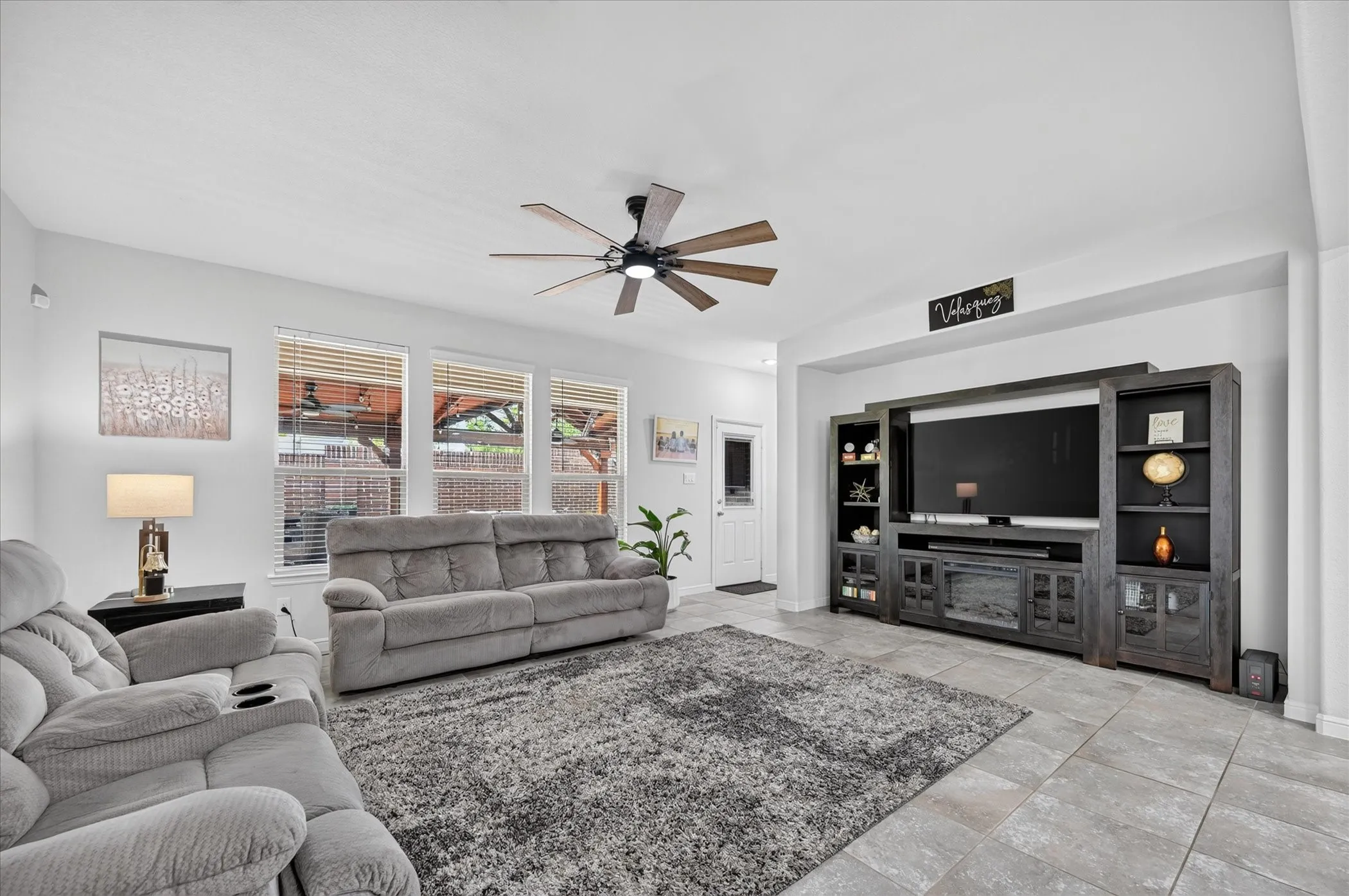 Tile flooring, ceiling fan with integrated lighting, three windows with blinds, recessed wall feature, and a white door