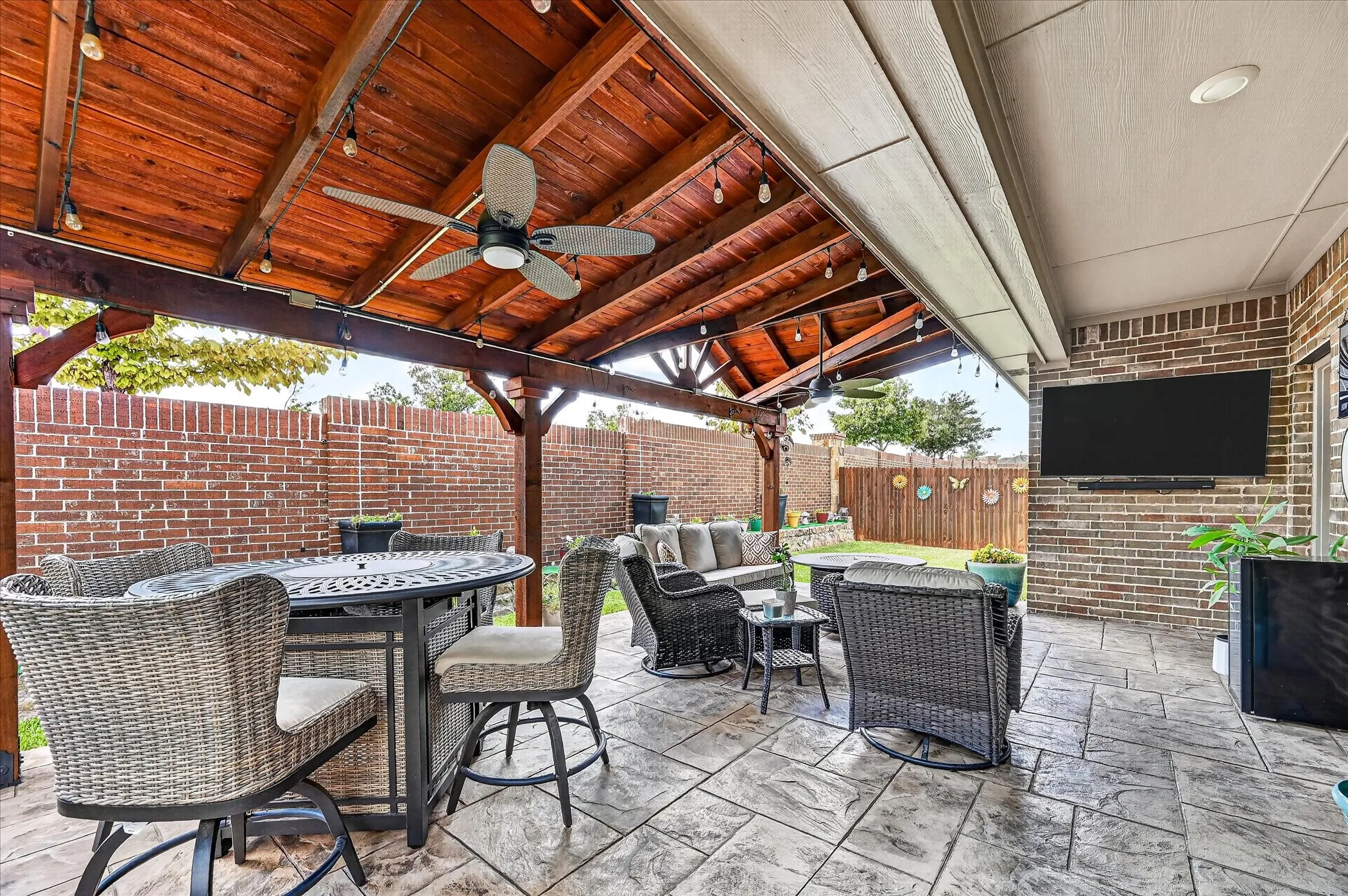 Covered patio featuring an exposed wood beam ceiling, stamped concrete flooring, brick privacy walls, and a ceiling-mounted fan