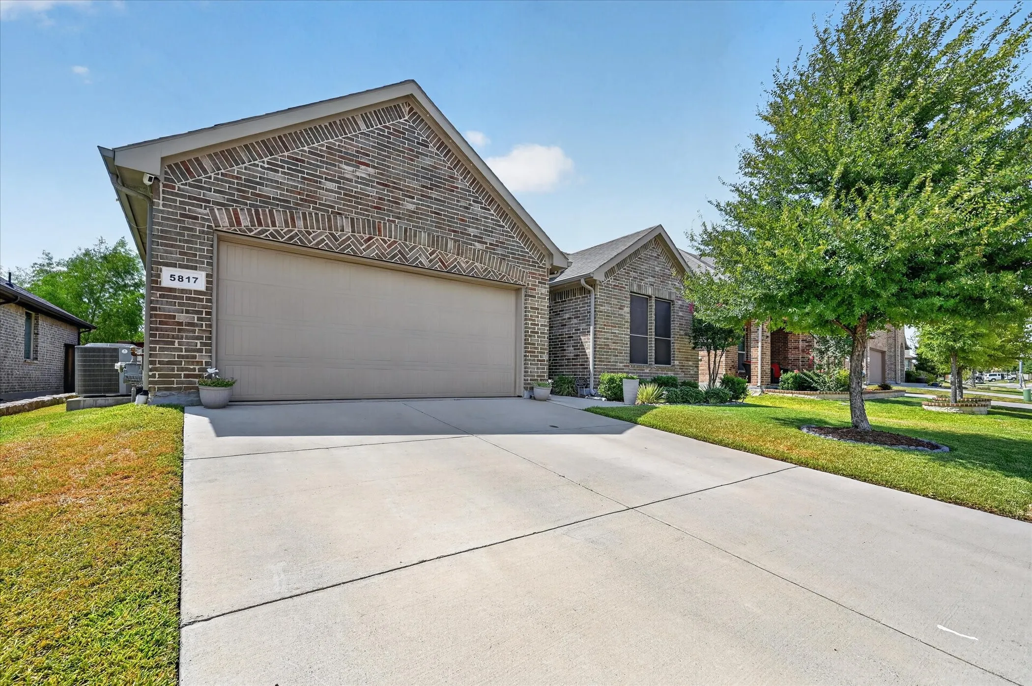 Brick exterior with decorative brickwork accents, attached garage, concrete driveway, and landscaped front yard