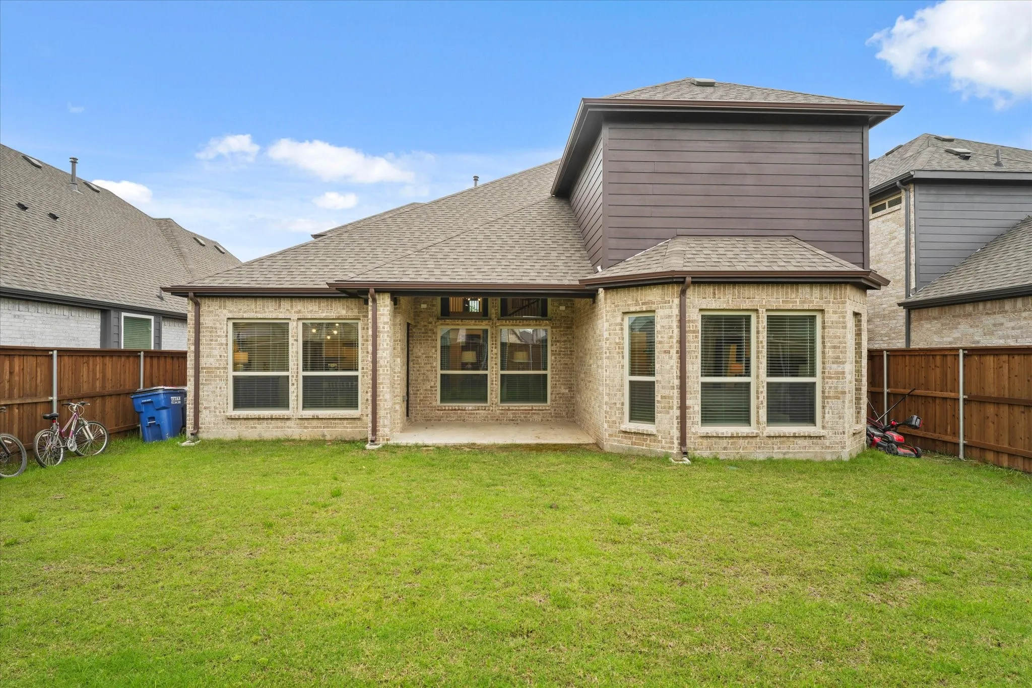Expansive backyard featuring a manicured lawn, full brick exterior, large windows, and a covered patio