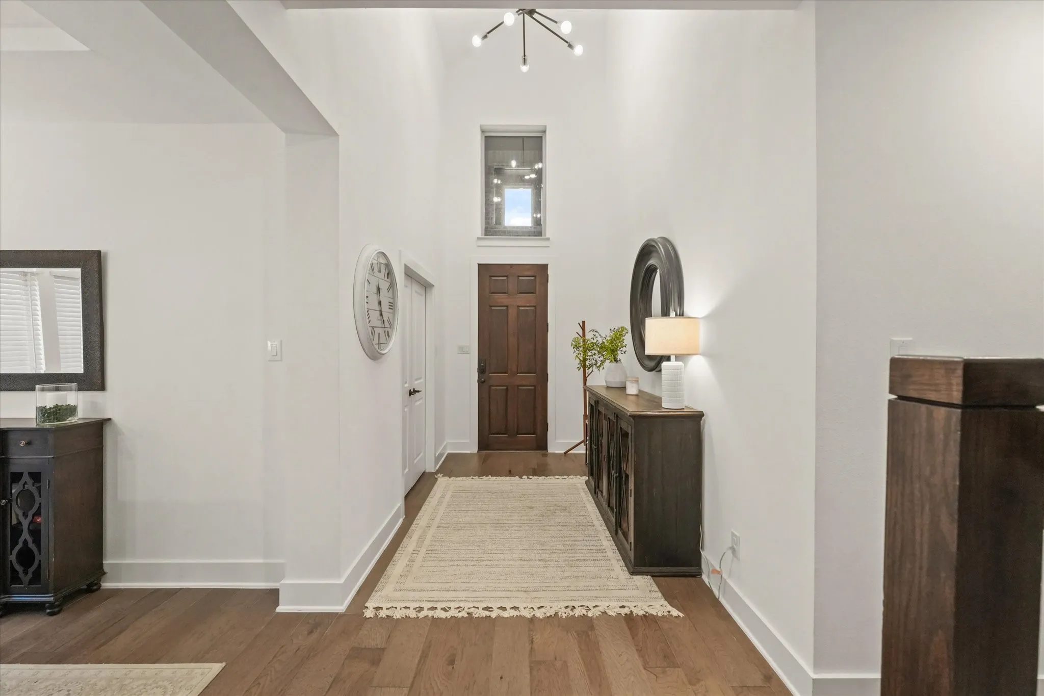 Hardwood flooring throughout, high ceilings, wood-paneled door, and a modern chandelier