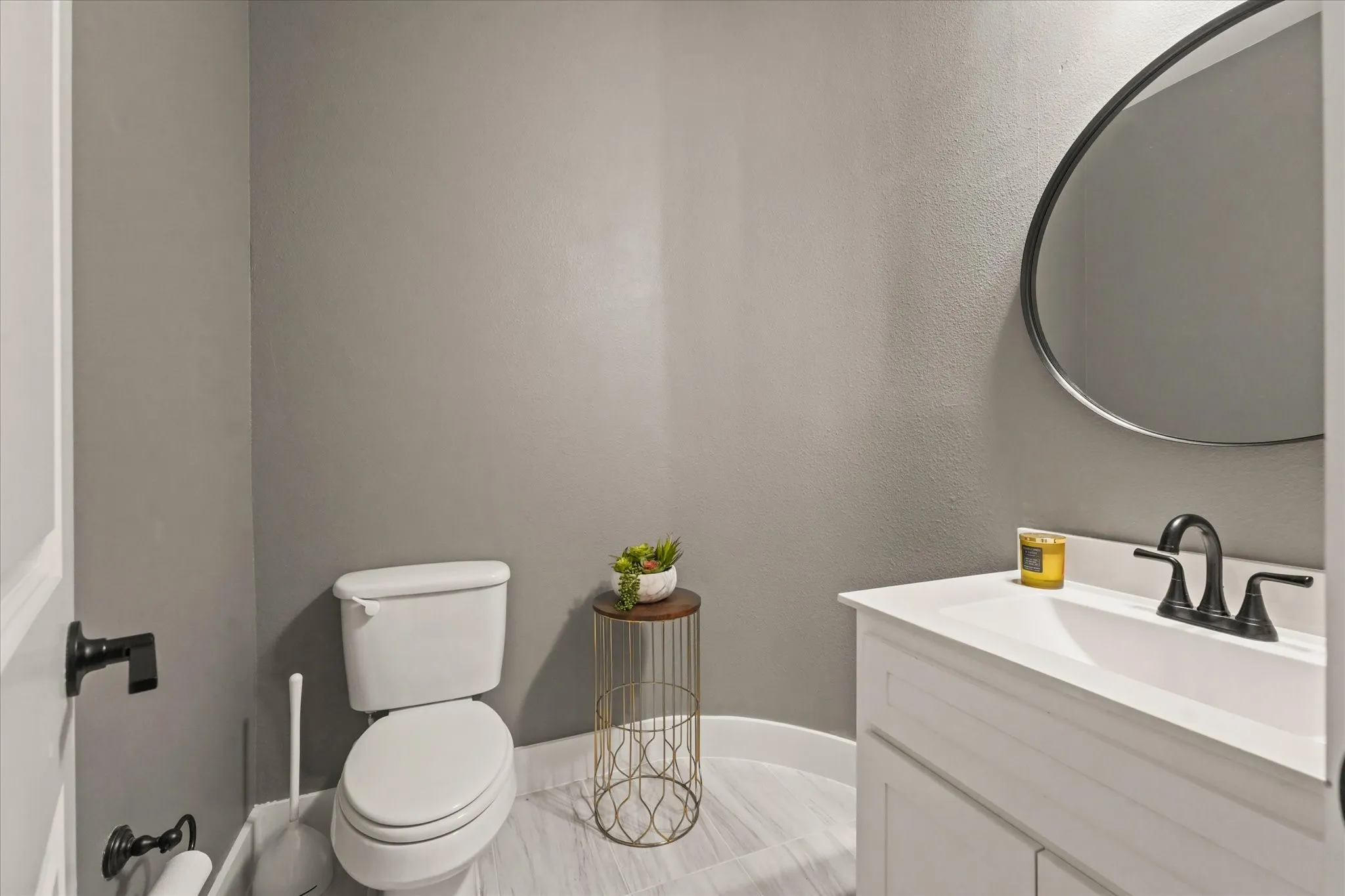 Elegant powder room featuring a white ceramic toilet, floating vanity with white cabinetry and a rectangular sink basin, matte black faucet hardware, tile flooring, and a framed oval mirror