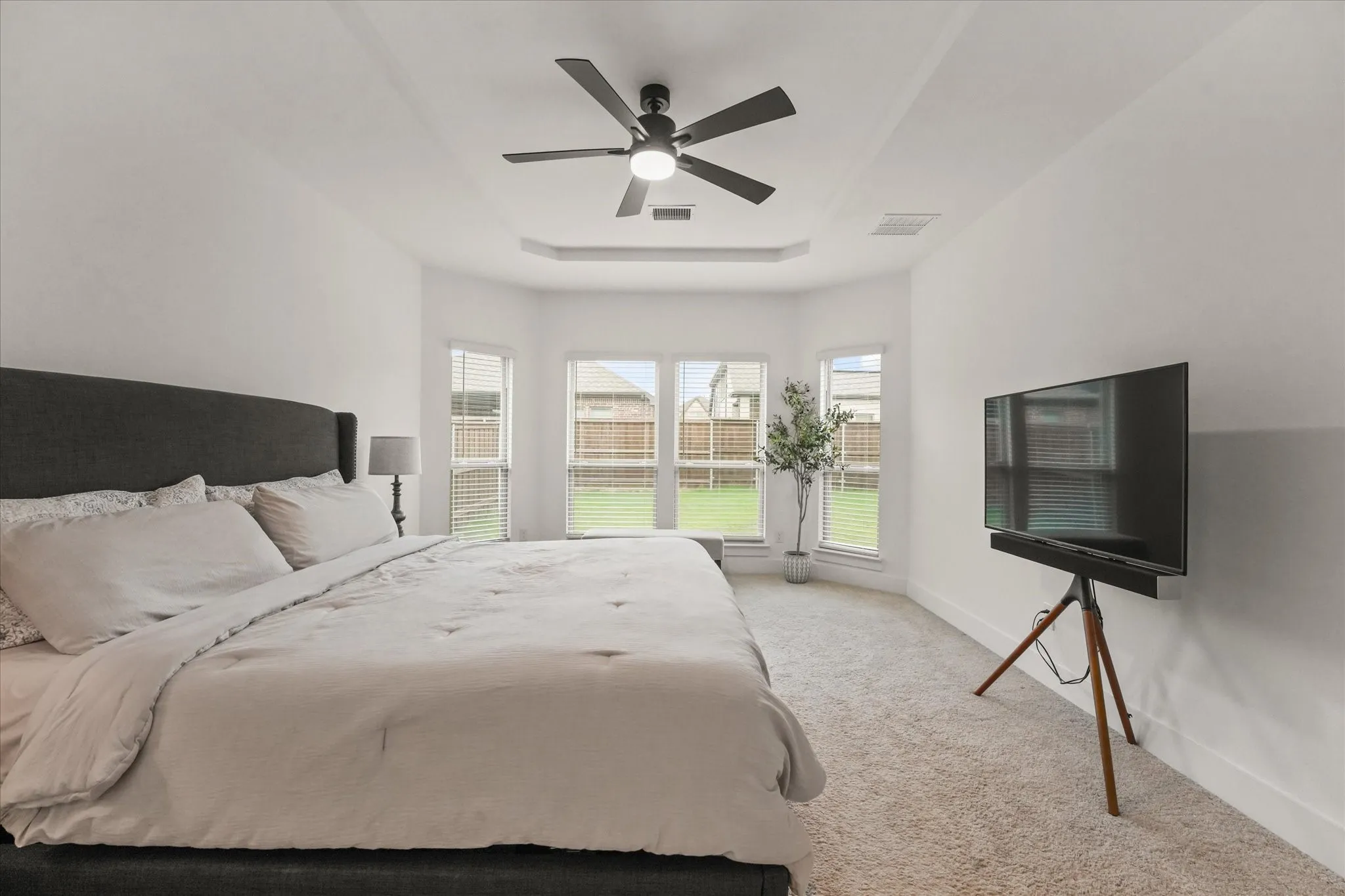 Tray ceiling with a ceiling fan, bay window, and carpeted flooring