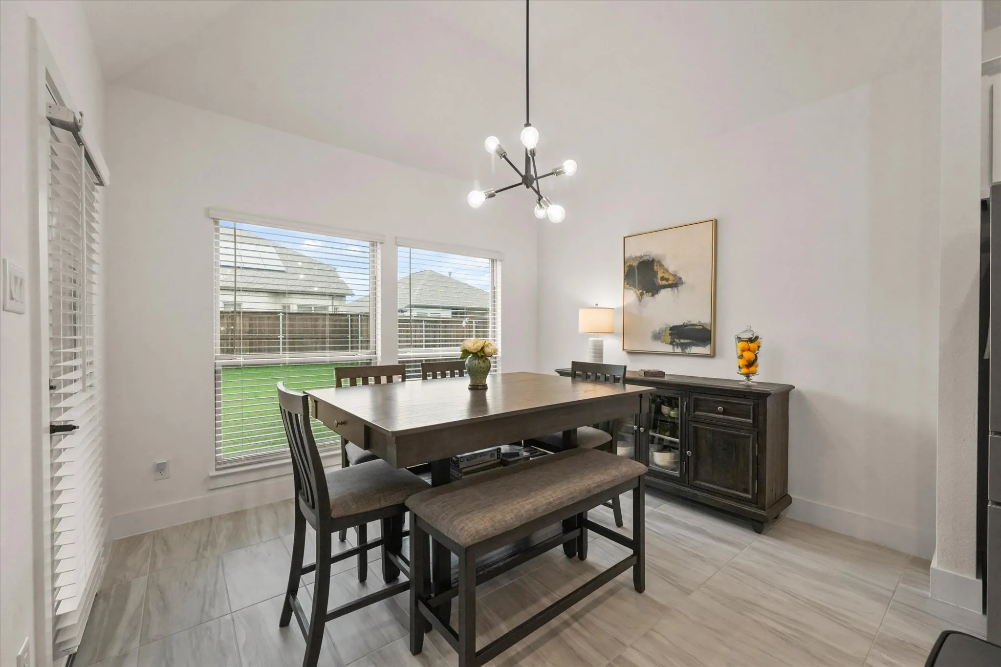 Recessed lighting and a modern linear chandelier illuminate a bright interior with tile flooring