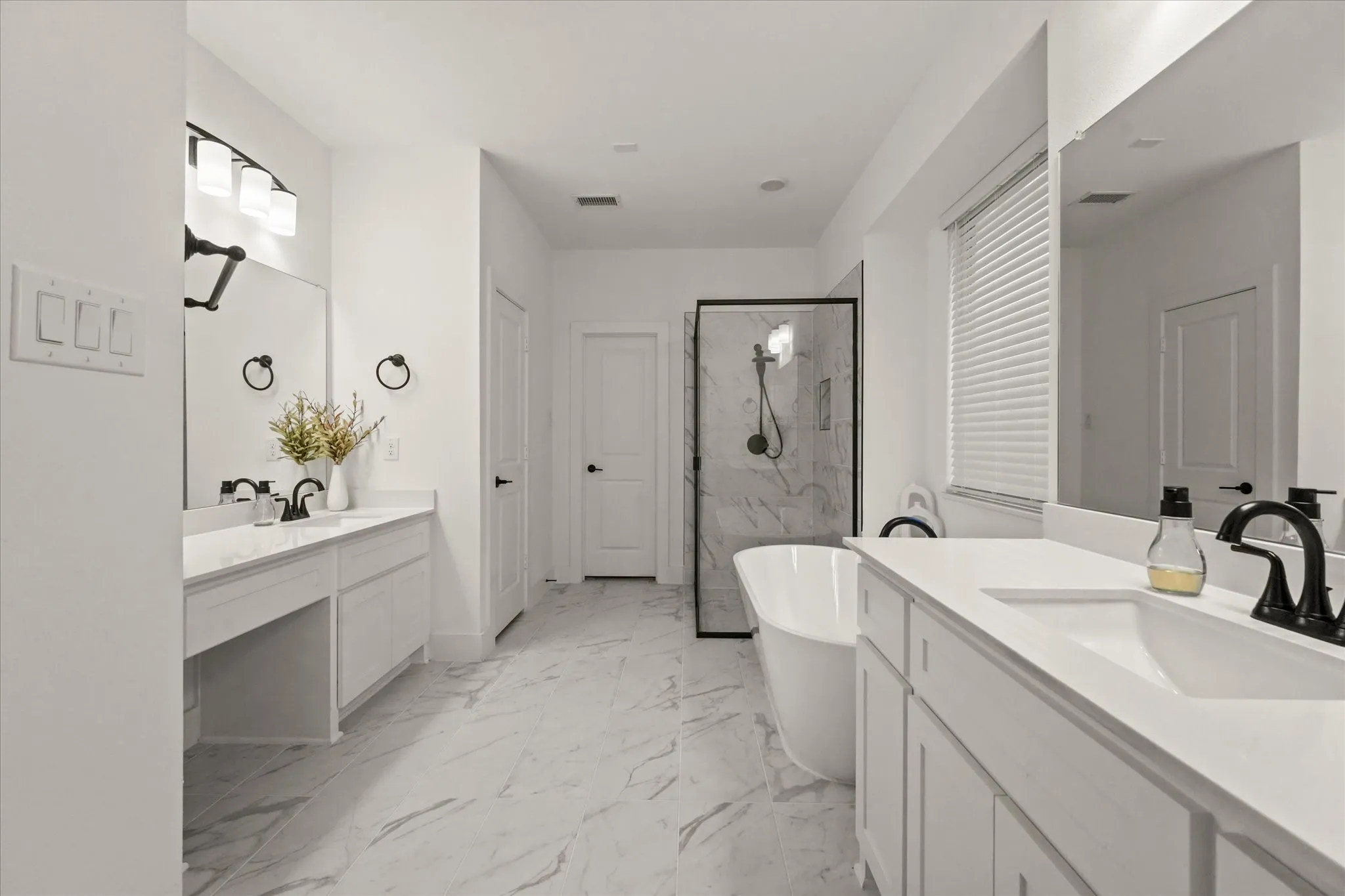 Dual vanity with undermount sinks, freestanding bathtub, glass-enclosed shower, and stone-finish flooring