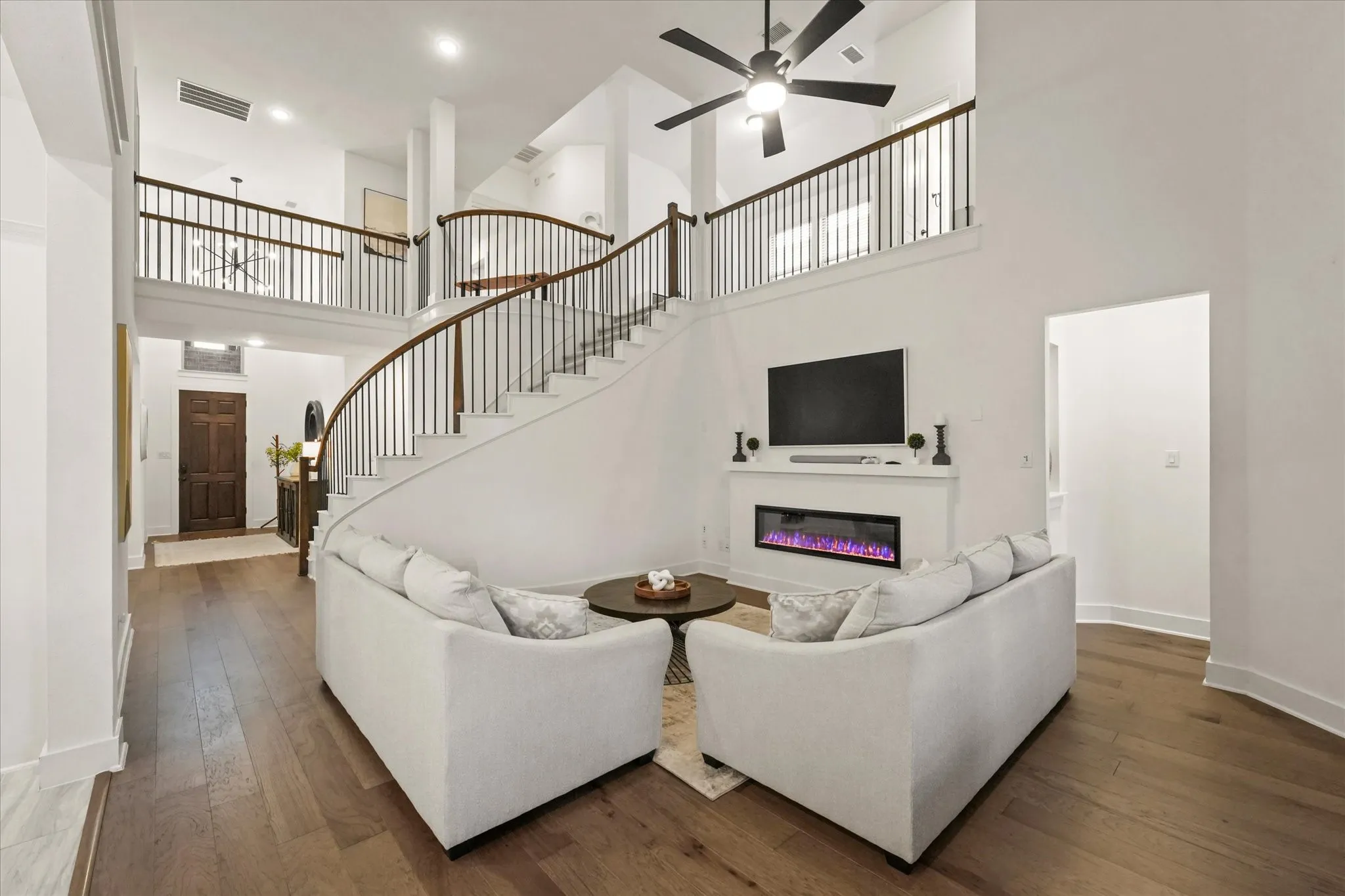 Soaring ceilings with a decorative ceiling fan, wood-finish flooring, and a contemporary fireplace with a mantel