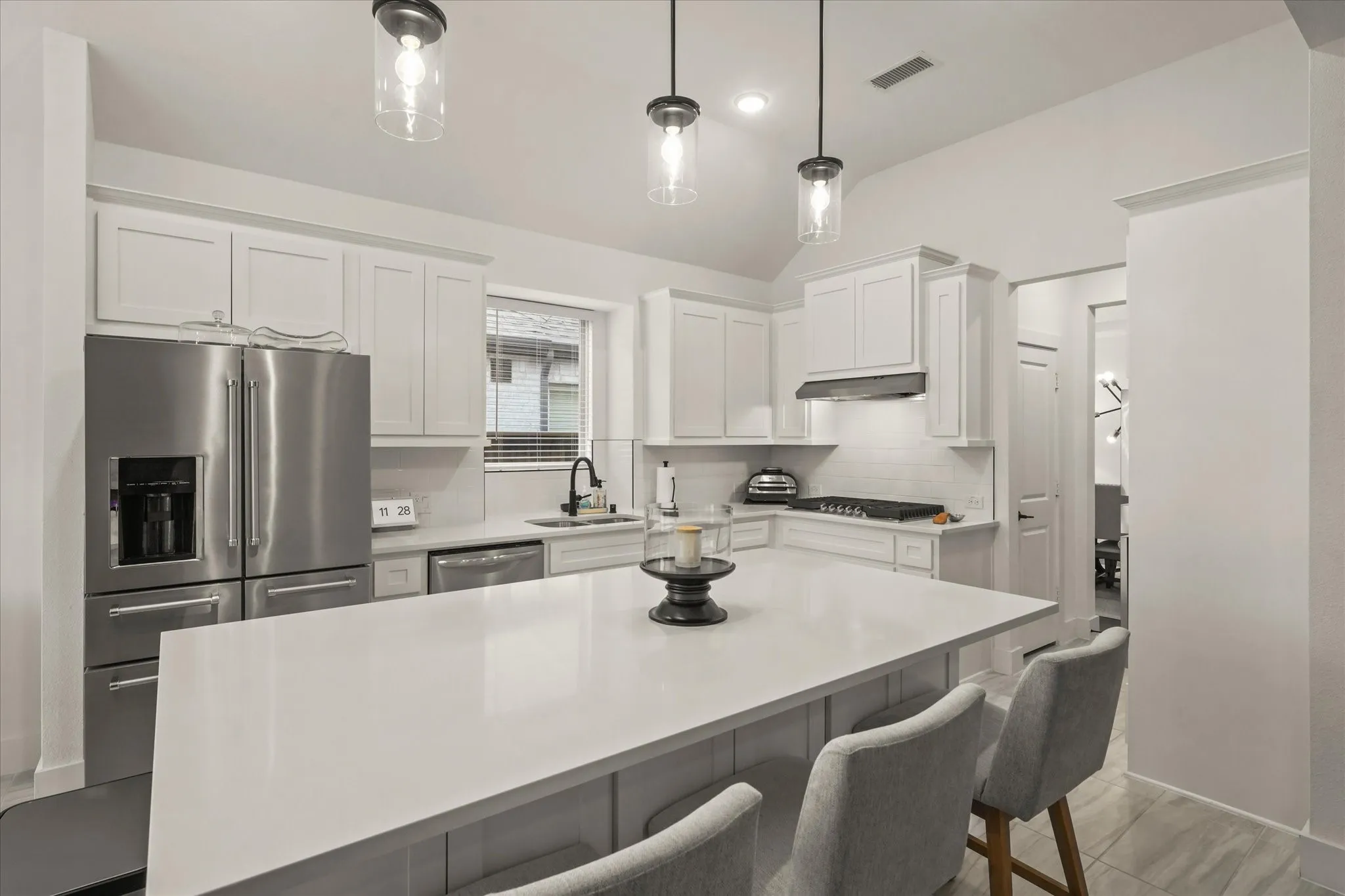 Bright kitchen featuring white shaker cabinetry, stainless steel appliances, a center island with countertop seating, and pendant lighting