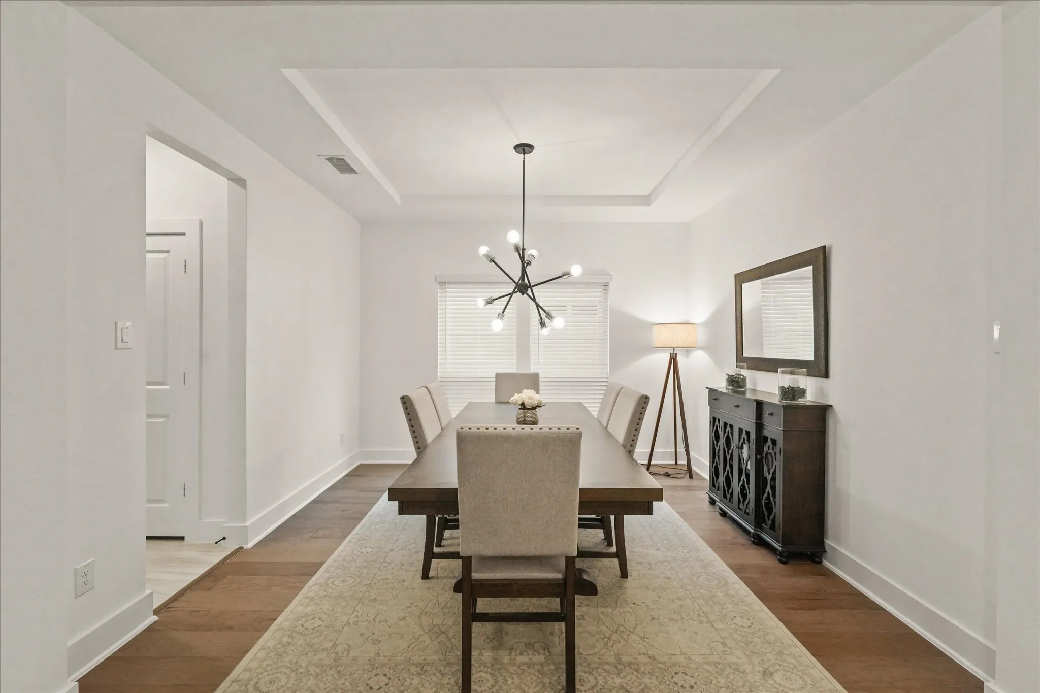 Recessed tray ceiling with chandelier, wood-finish flooring, white window blinds, and white interior walls