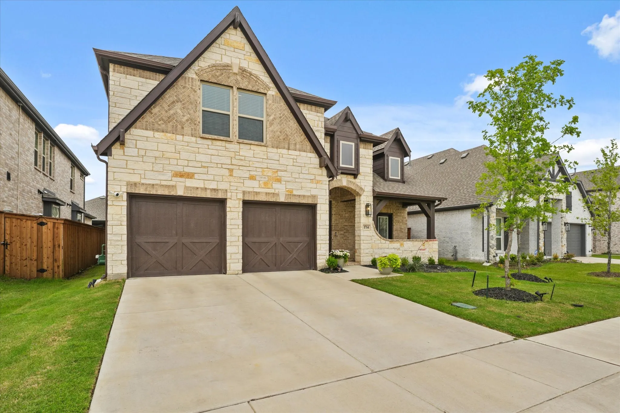 Stone and brick facade with a prominent gabled roofline, two-car garage with wood-finish doors, covered entry porch, and a concrete driveway
