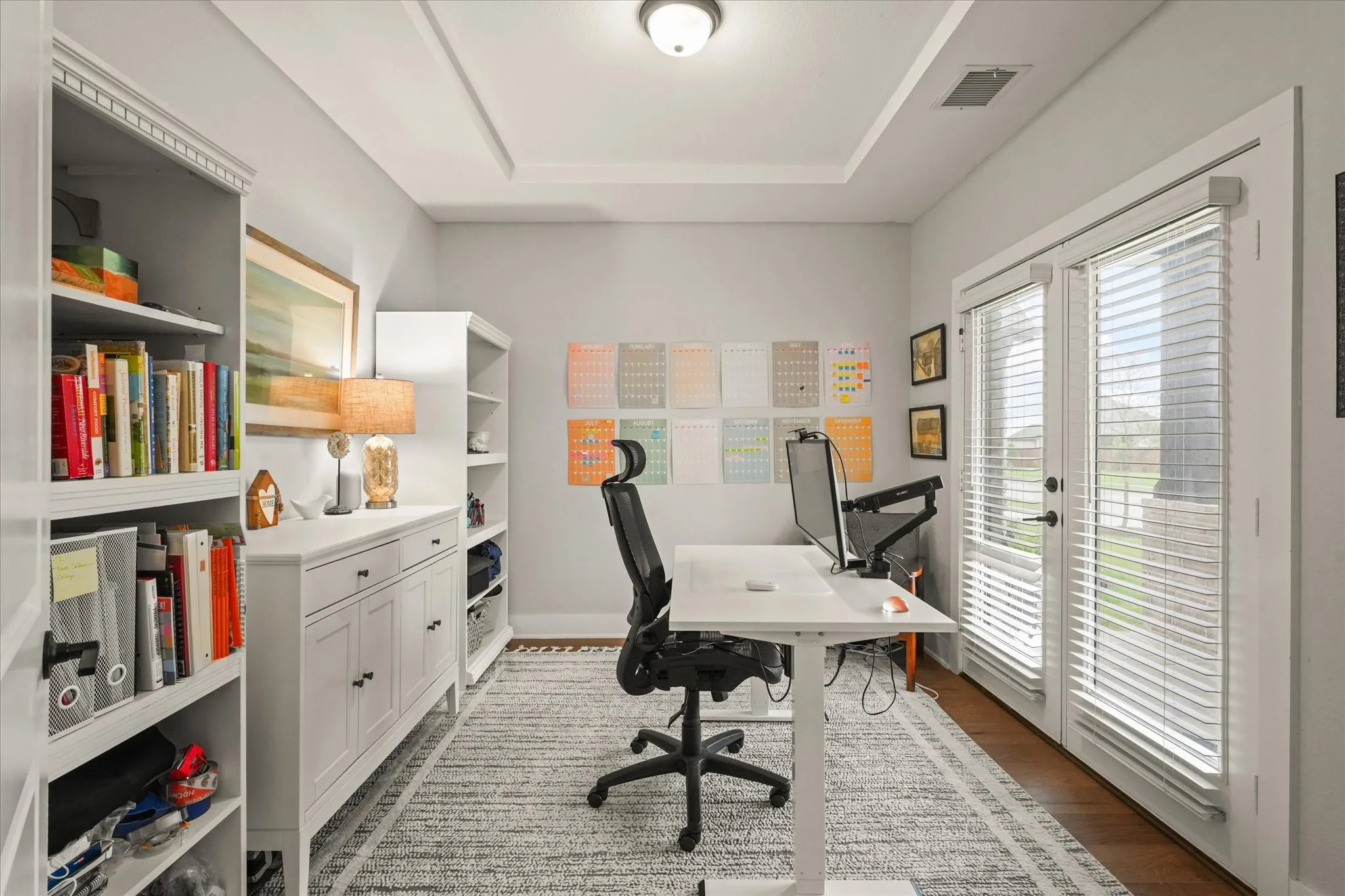 Tray ceiling with recessed lighting, wood-finish flooring, and white built-in shelving