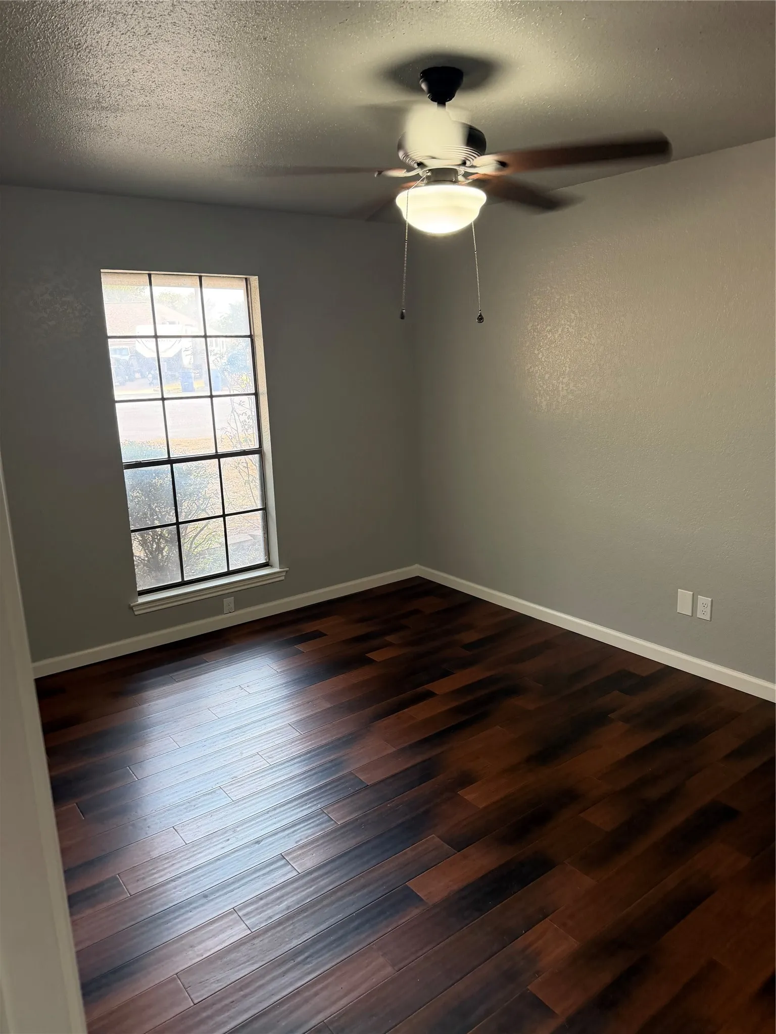 Wood-finish flooring, ceiling fan with integrated lighting, window with grid pattern, and light-toned walls
