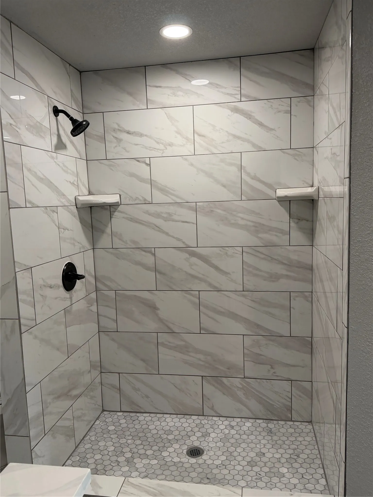Shower featuring large format wall tiling, hexagonal floor tiling, recessed lighting, and matte black fixtures