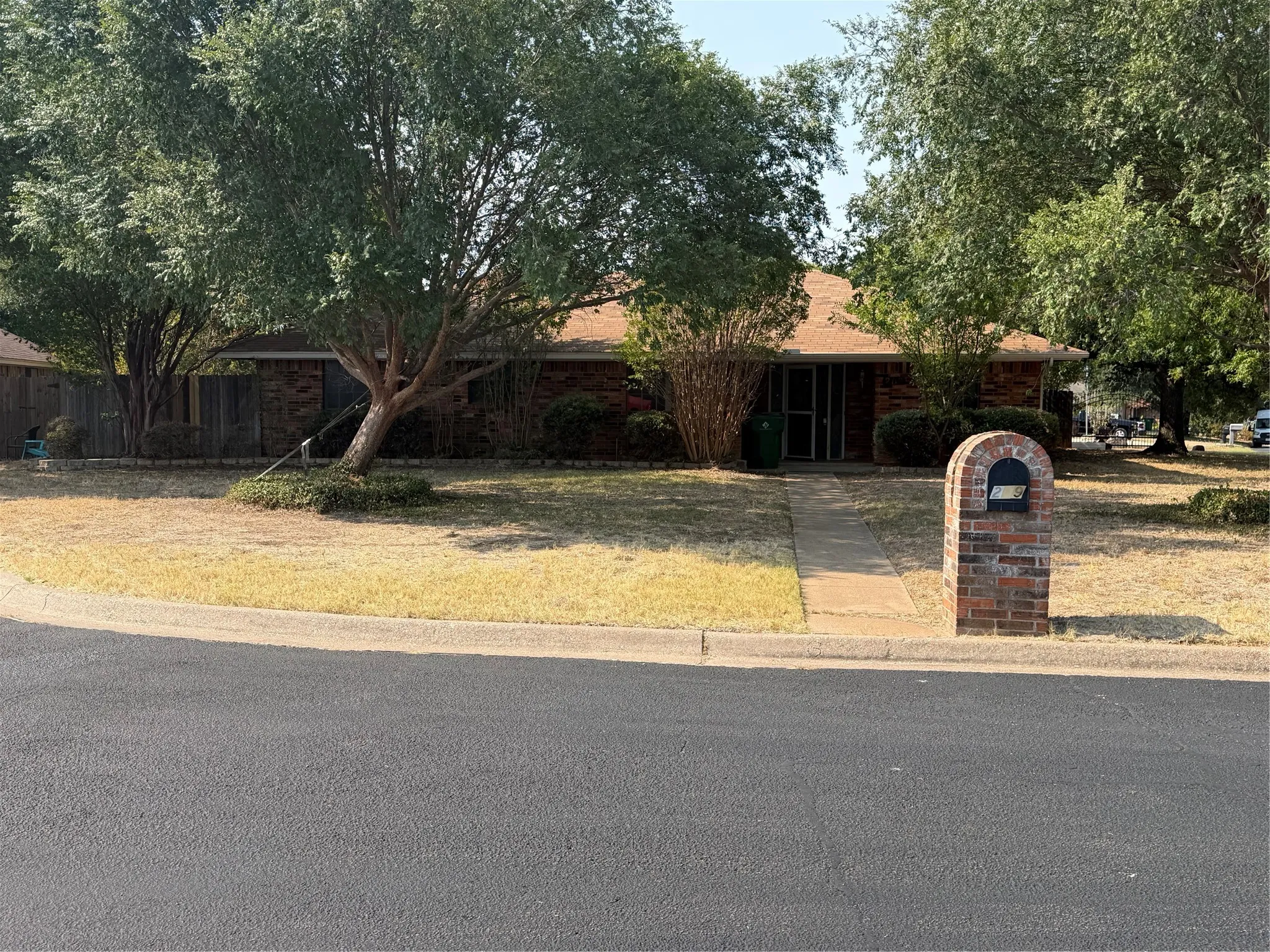 Brick exterior, shingle roof, mature trees, sidewalk, and brick mailbox structure