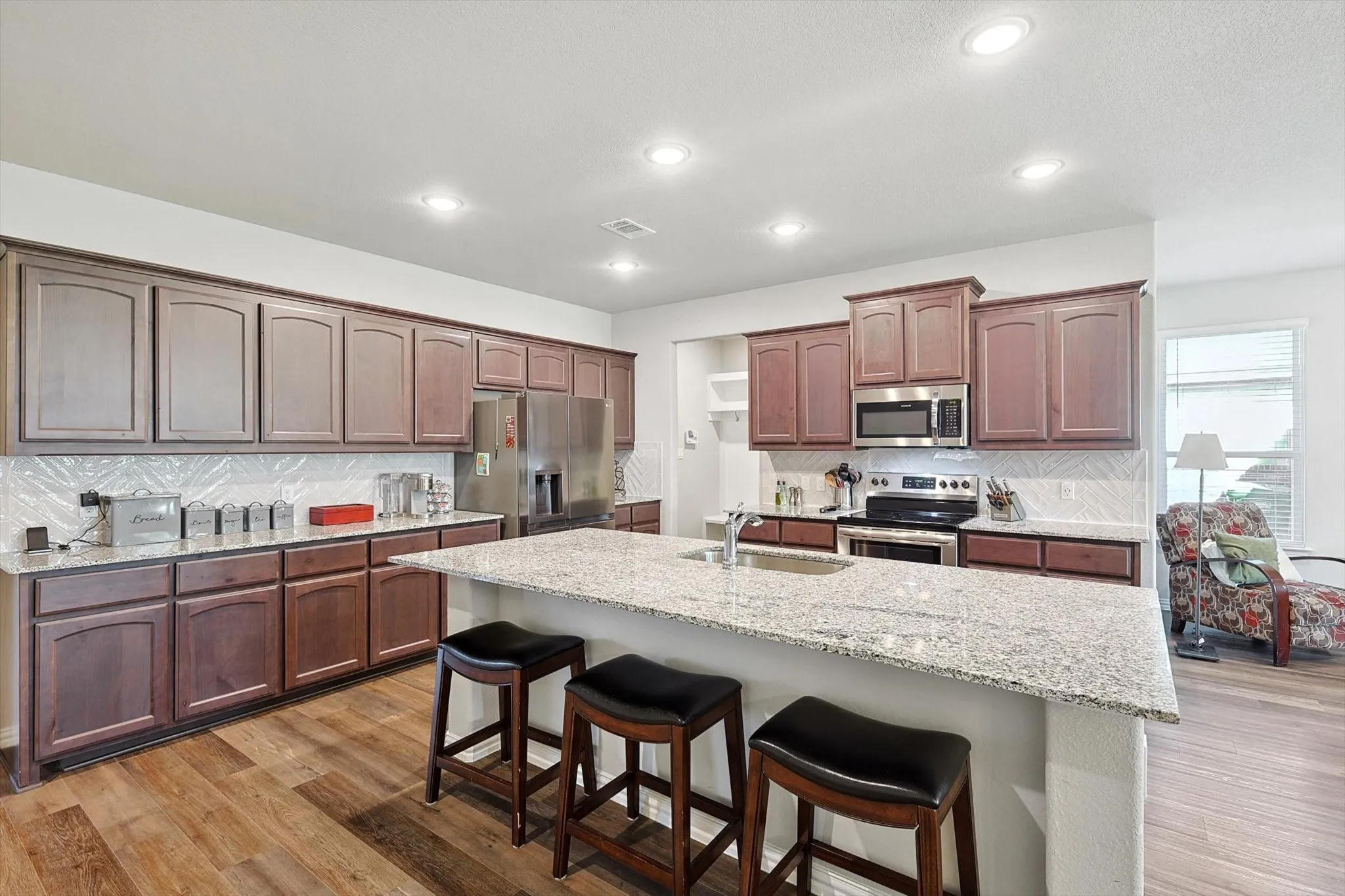 Kitchen featuring wood-finish flooring, recessed lighting, expansive island with an undermount sink, stone countertops, and stainless steel appliances