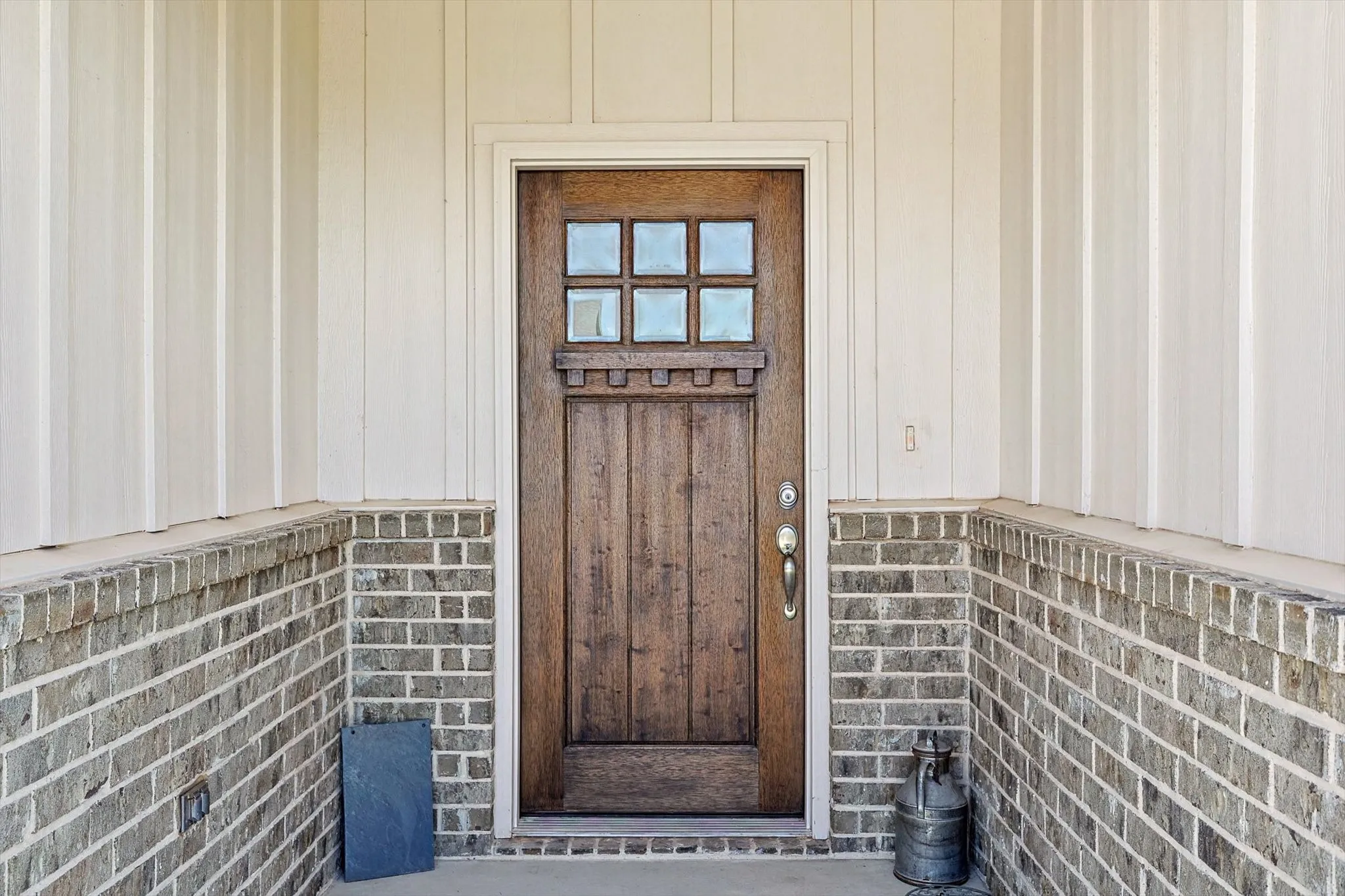 Wood-finish entry door with clear glass panels, board and batten siding, and brick veneer detailing