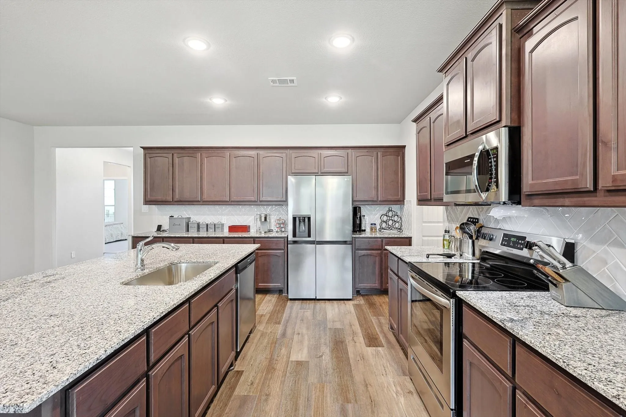 Expansive kitchen with granite countertops, wood-finish flooring, stainless steel appliances, and abundant cabinetry
