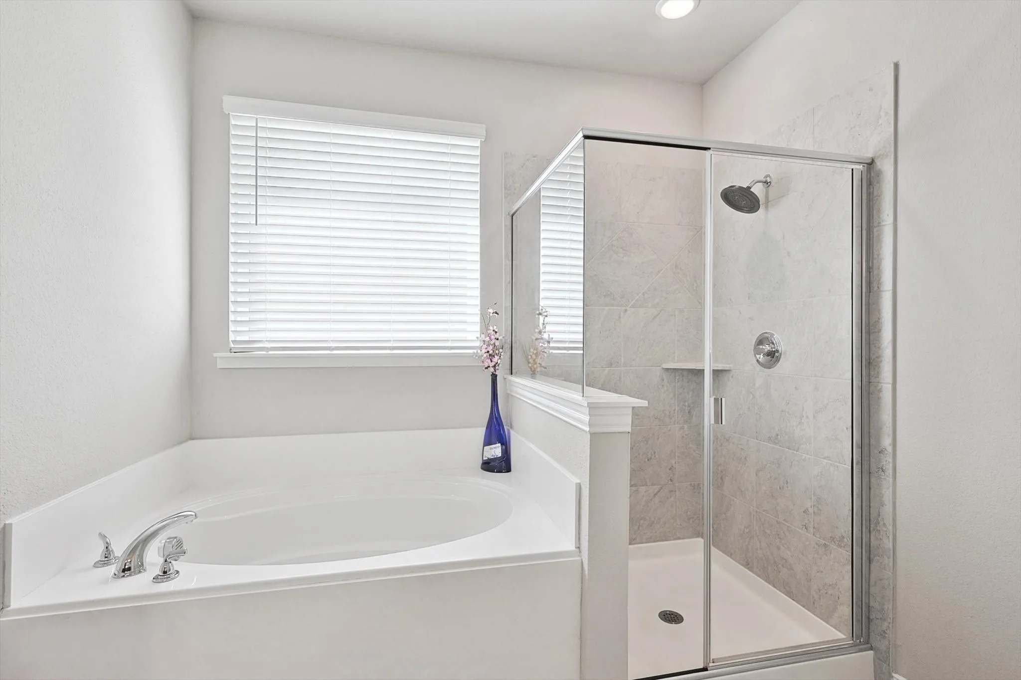 Soaking tub with deck-mounted chrome fixtures, adjacent to a glass-enclosed shower with tile surround and rain shower head