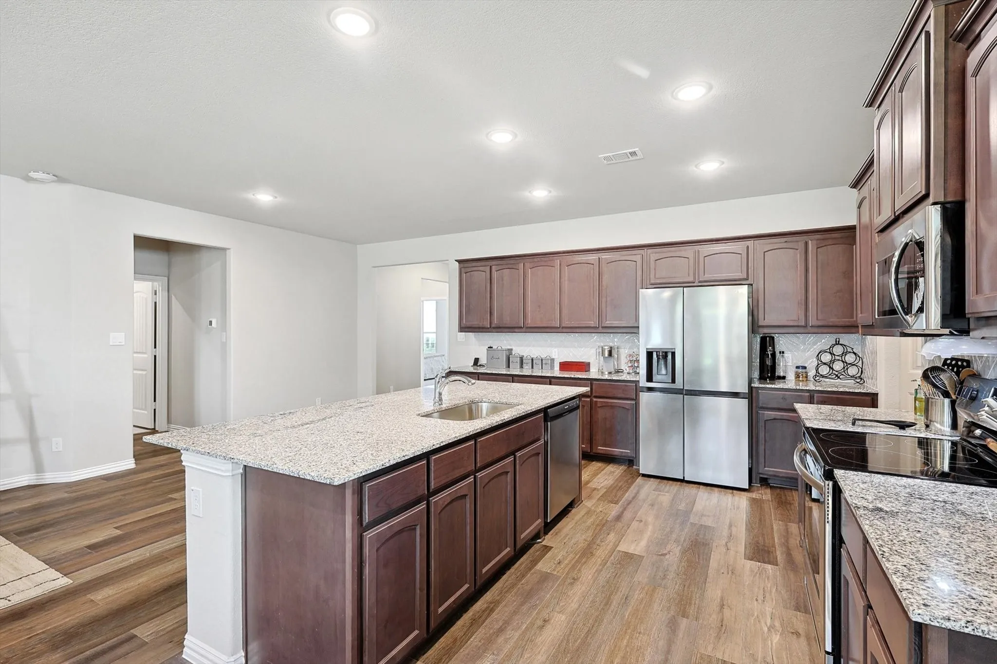 Kitchen featuring a large central island with an integrated sink, granite countertops, wood-finish flooring, recessed lighting, and stainless steel appliances
