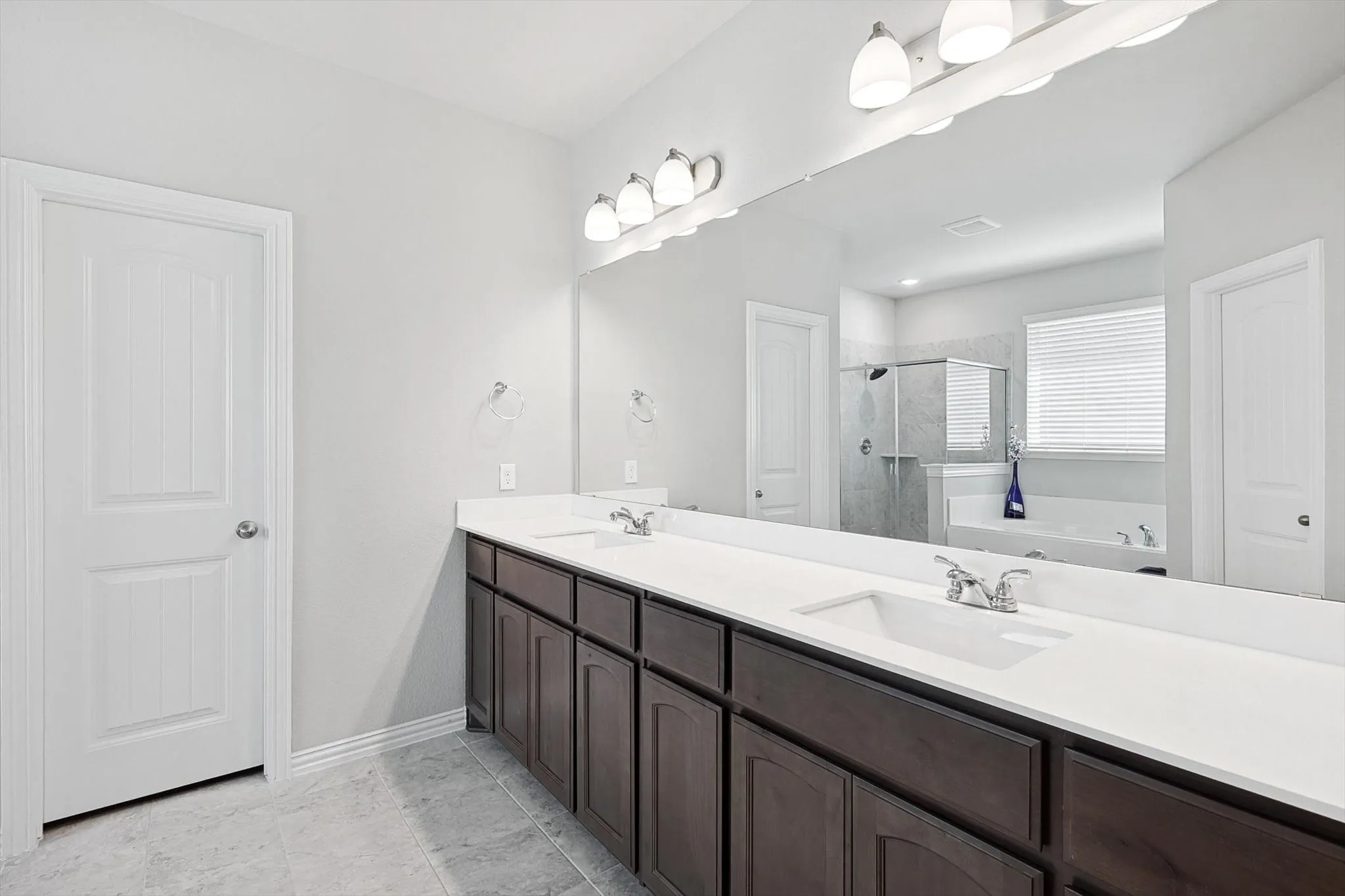 Dual vanity with white countertops, dark wood-finish cabinetry, and an expansive mirror