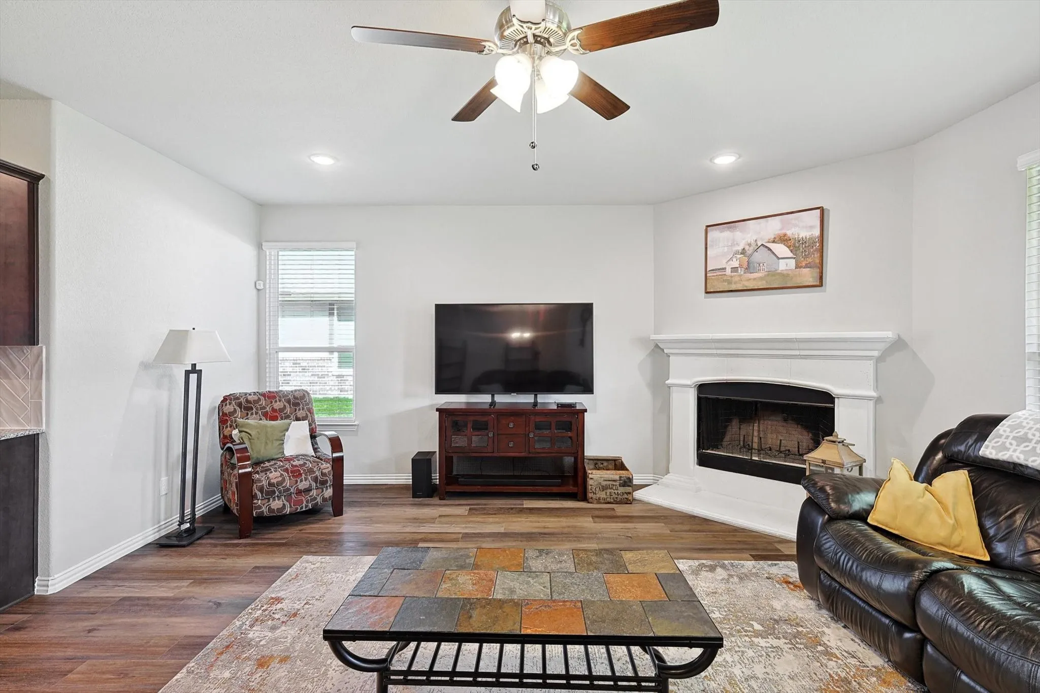 Wood-finish flooring, recessed lighting, ceiling fan with light, and a fireplace with a mantel