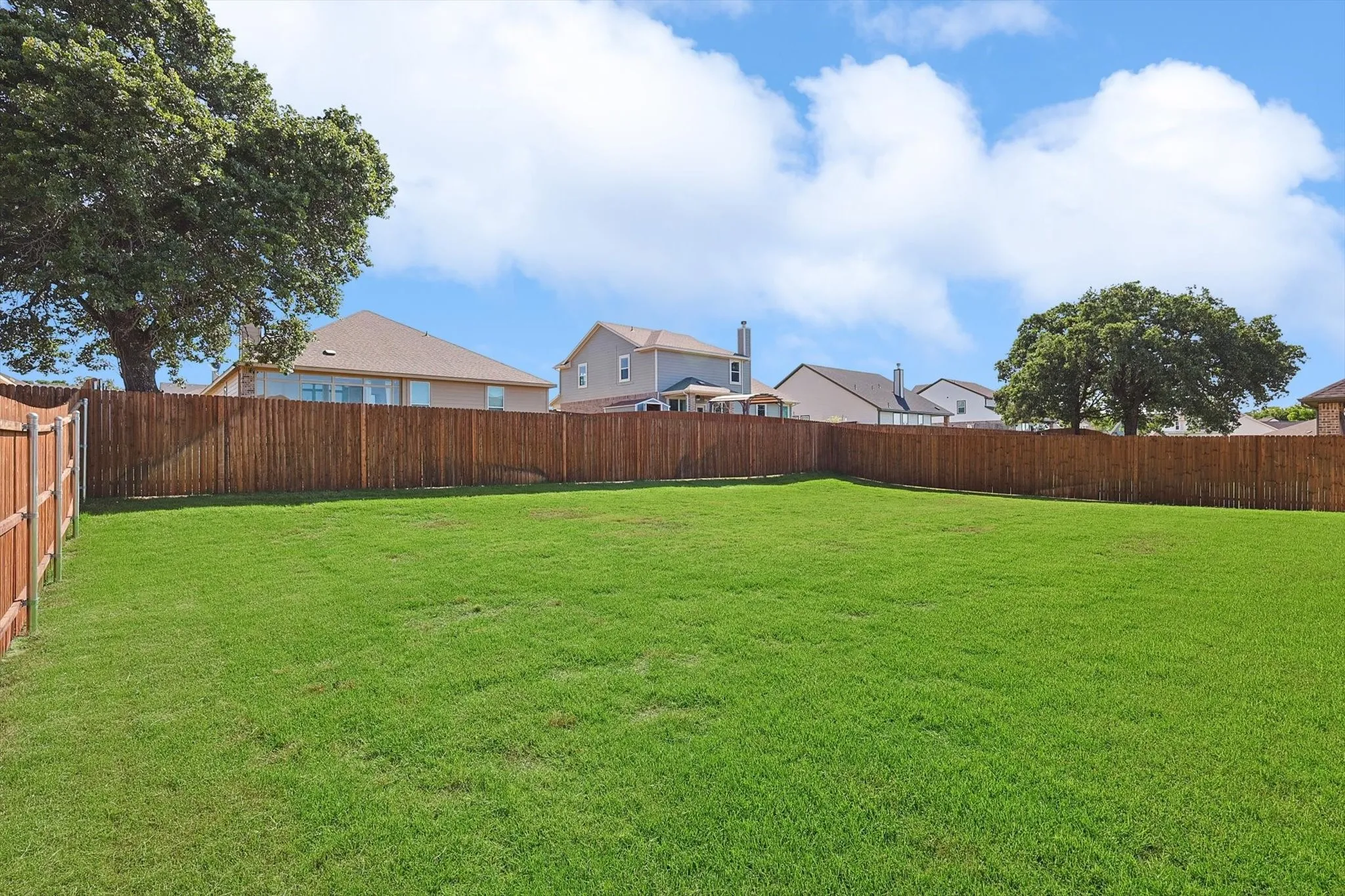 Expansive backyard featuring a lush lawn, privacy fencing, and mature trees