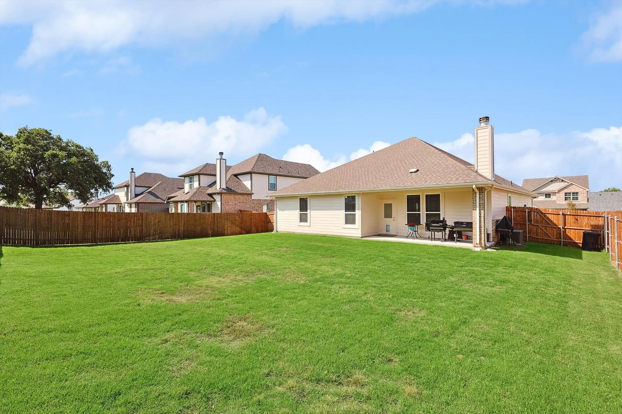 Expansive backyard featuring a manicured lawn, full wood privacy fencing, a concrete patio, and a visible chimney structure