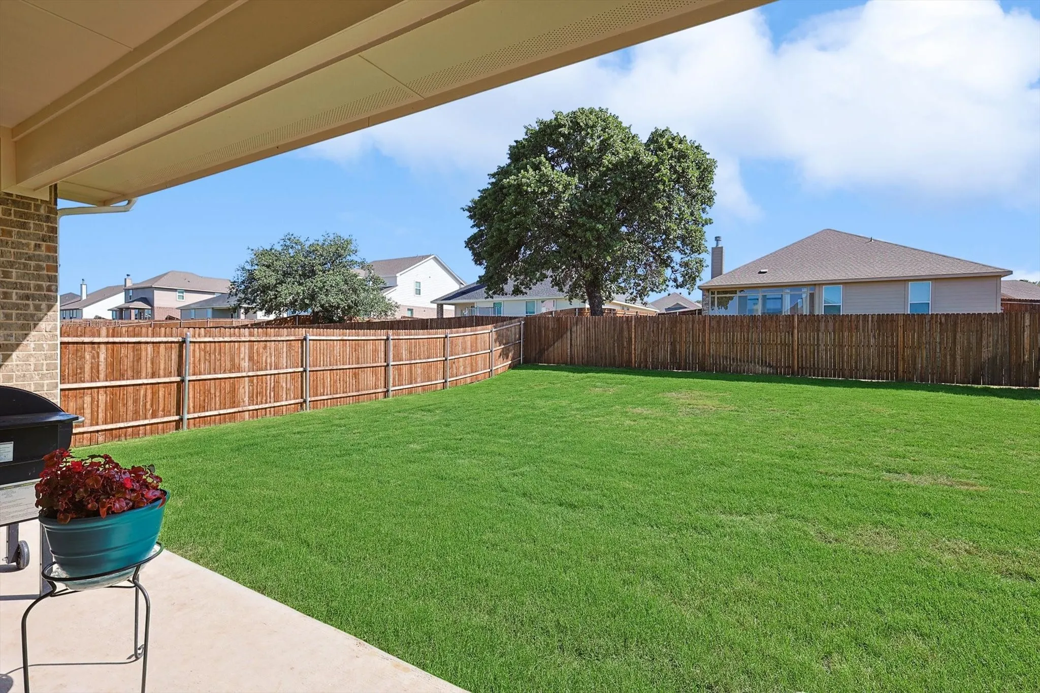 Covered patio with brick siding, concrete patio, expansive lawn, mature tree, and wood privacy fencing