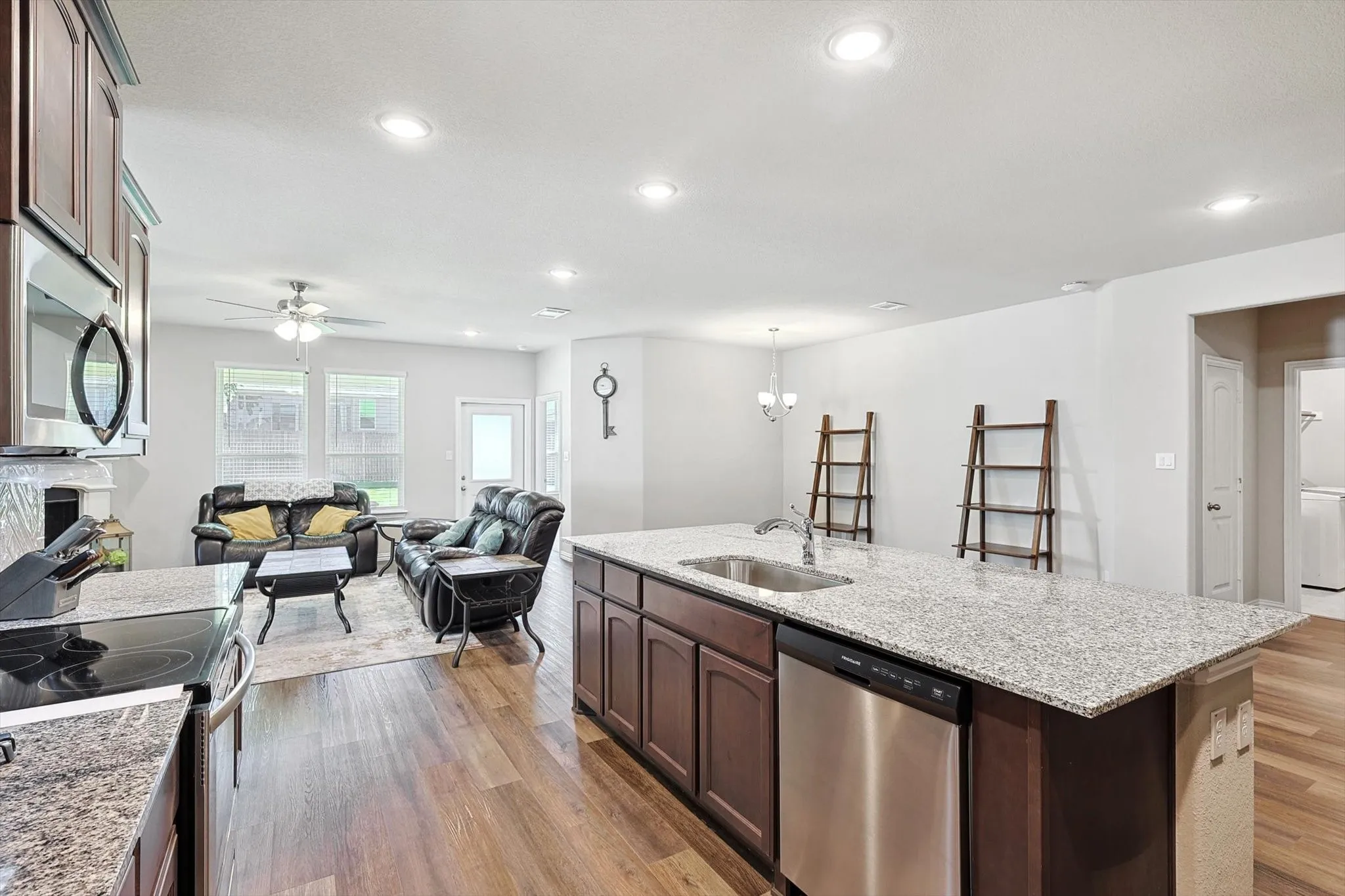 Open-concept living area featuring wood-finish flooring, a kitchen island with stone countertops and an undermount sink, recessed lighting, and stainless steel appliances