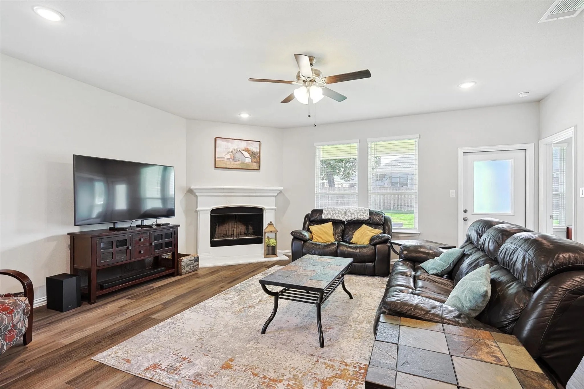 Spacious living area featuring wood-finish flooring, a corner fireplace with a white mantel, recessed lighting, and a ceiling fan