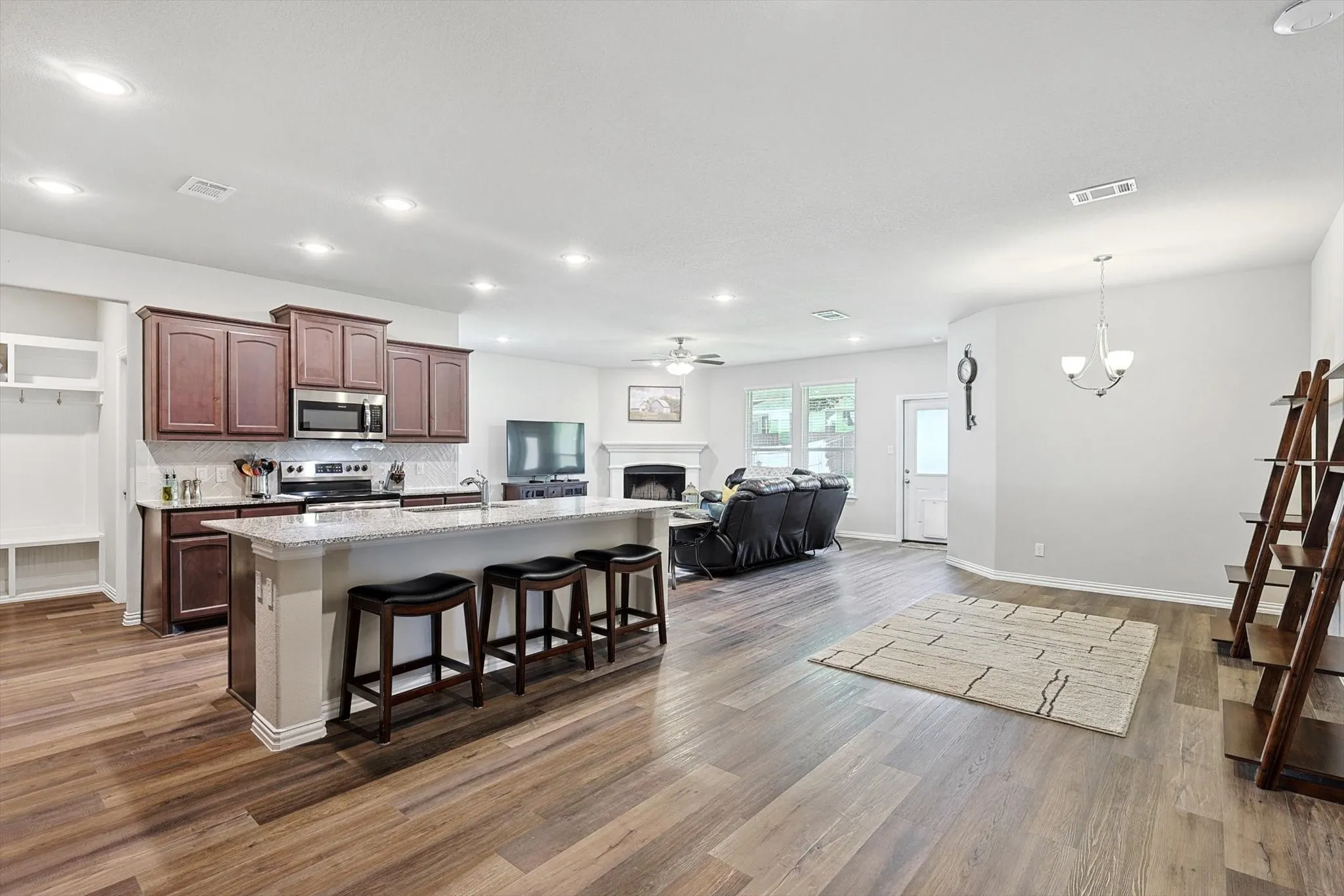 Open-concept interior with wood-finish flooring, recessed lighting, a kitchen island with seating, dark wood cabinetry, and a fireplace with a mantel