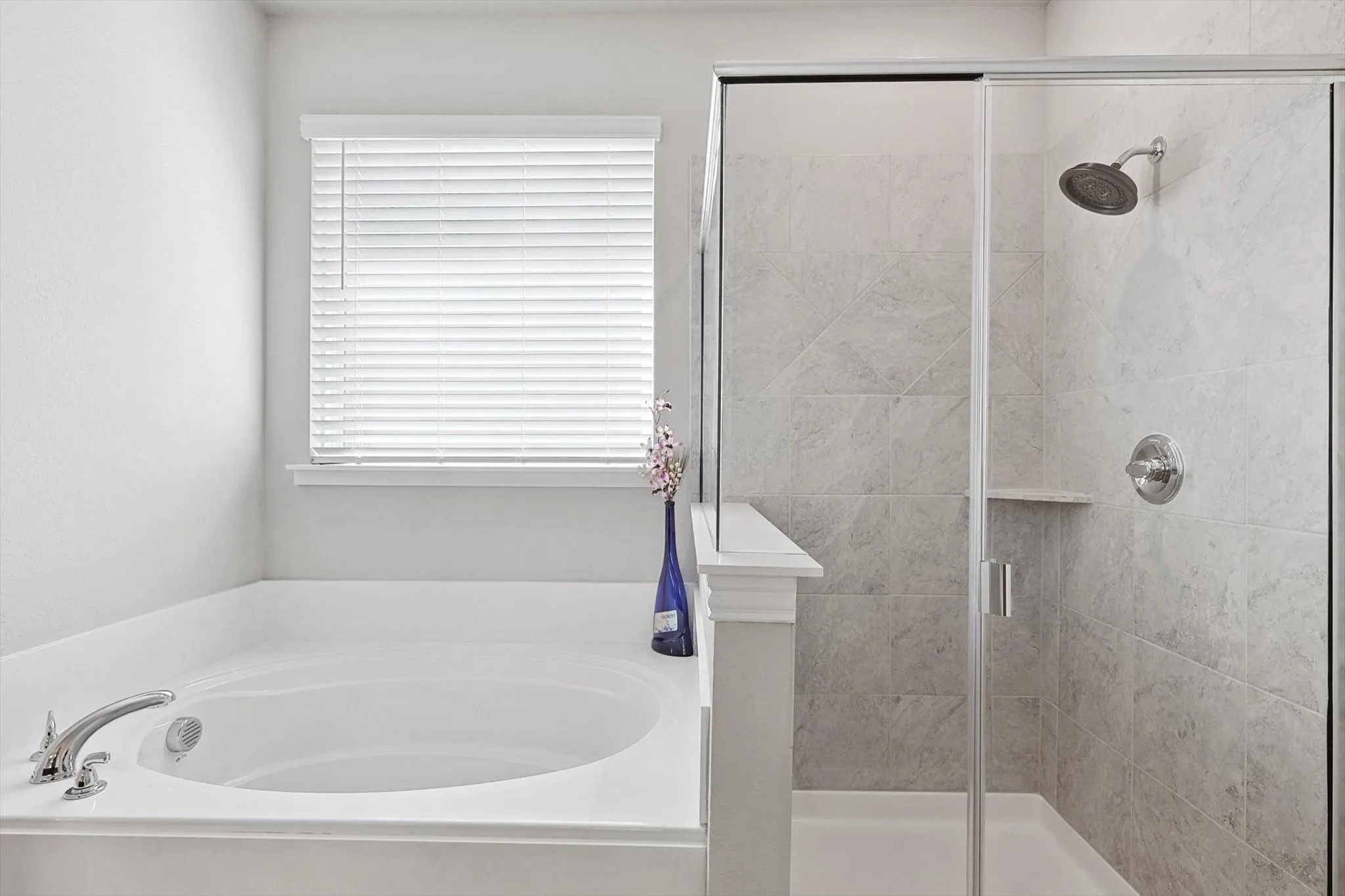 Built-in soaking tub with polished chrome fixtures, separate glass-enclosed shower, rain shower head, and light-toned tile surround