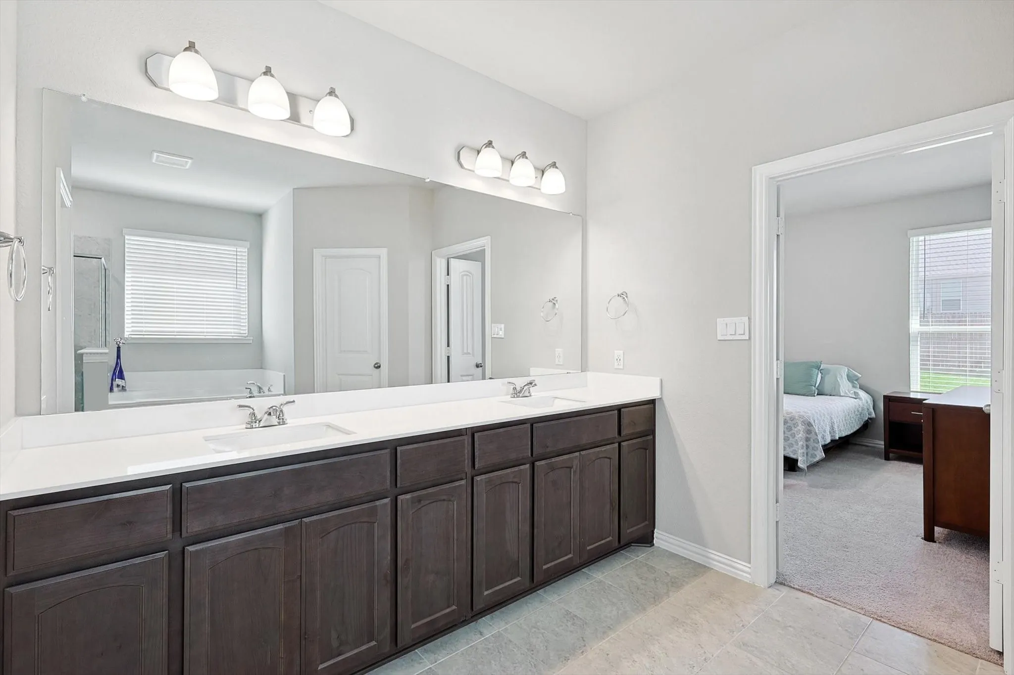 Dual vanity with white countertops, dark wood-finish cabinetry, a large frameless mirror, and overhead sconce lighting