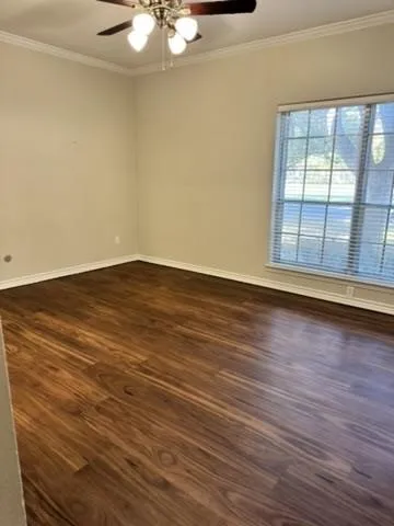 Wood-finish flooring, ceiling fan with light fixture, window with blinds, and crown molding