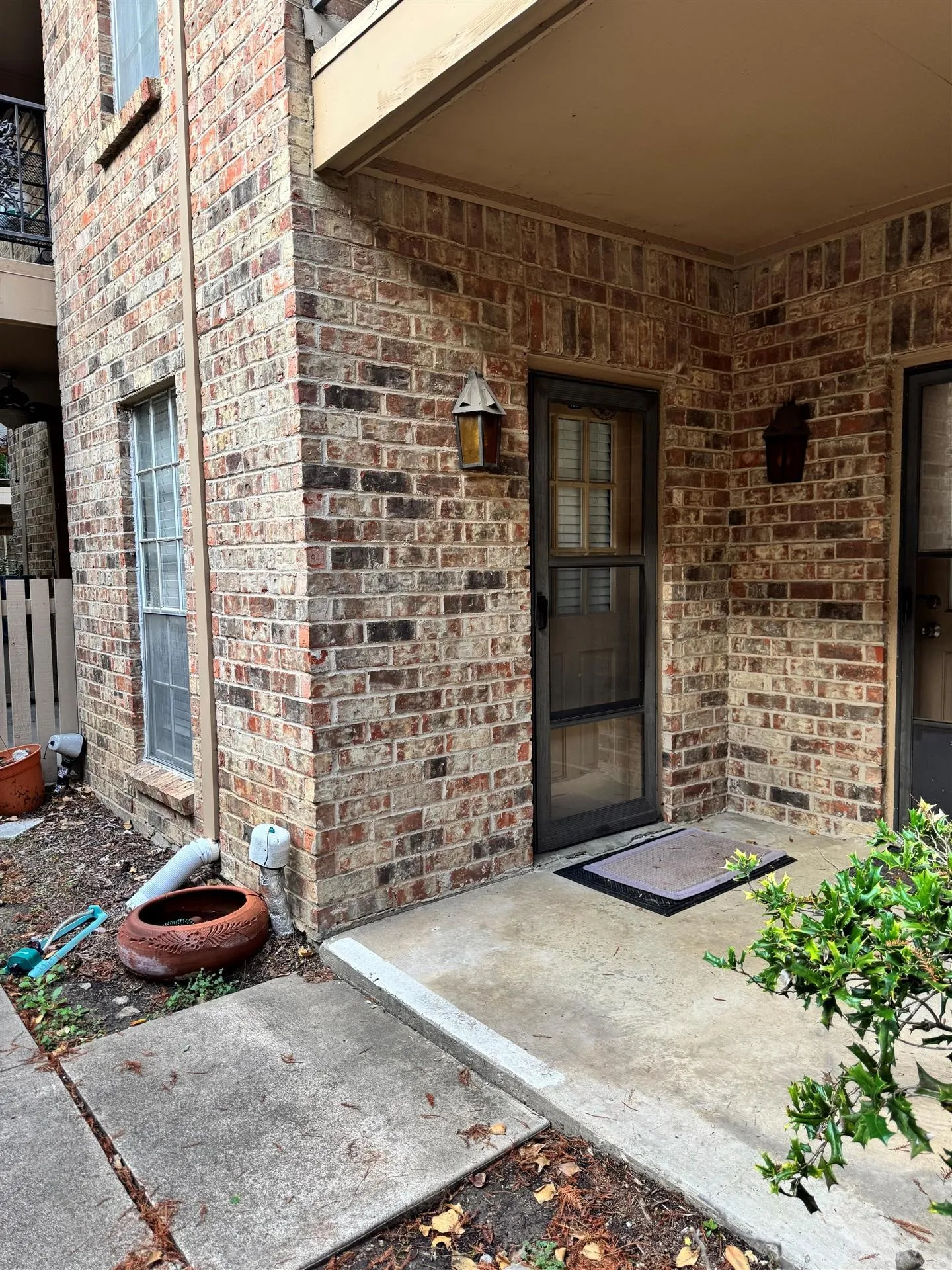 Brick exterior with a covered entry, exterior lighting fixture, and concrete walkway