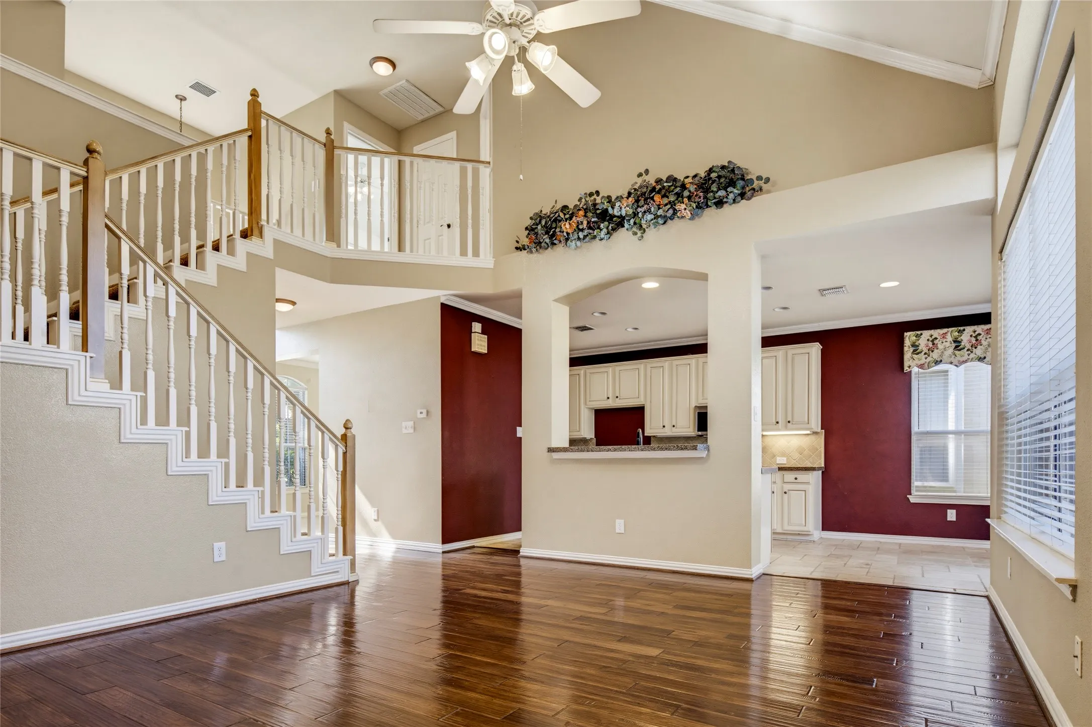 Soaring vaulted ceiling with a ceiling fan, wood-finish flooring, and a staircase with white balusters