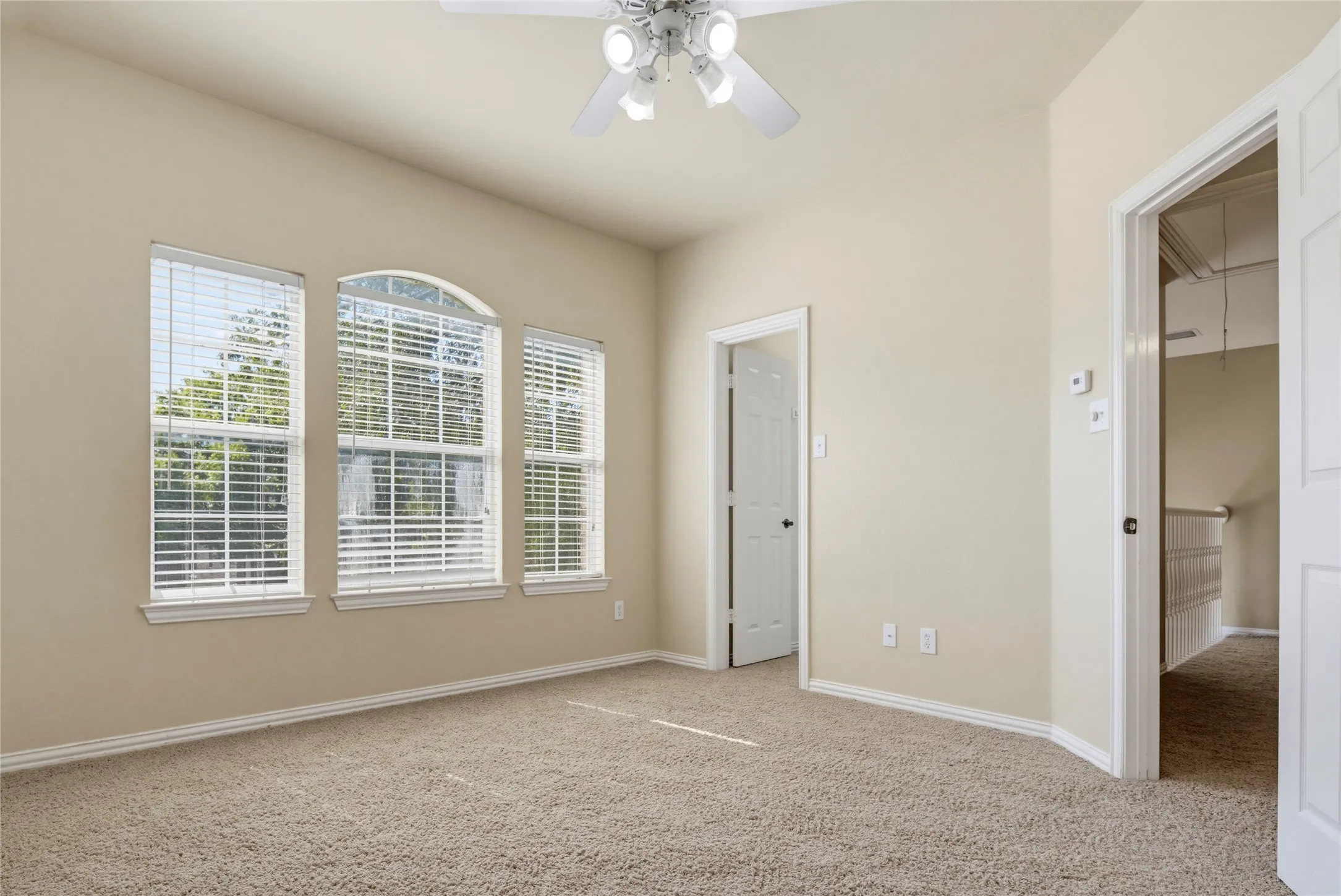 Vaulted ceiling with a ceiling fan, three windows, arched window, and carpet flooring