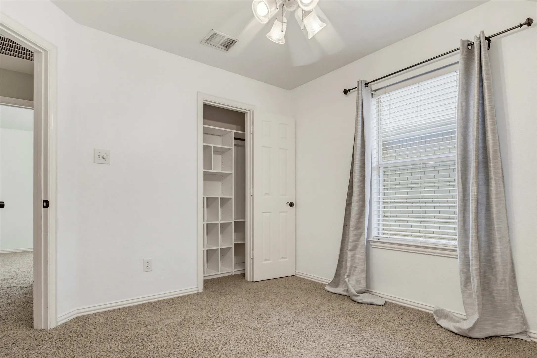 Carpeted room featuring a ceiling fan, a window with blinds, and a built-in closet organization system
