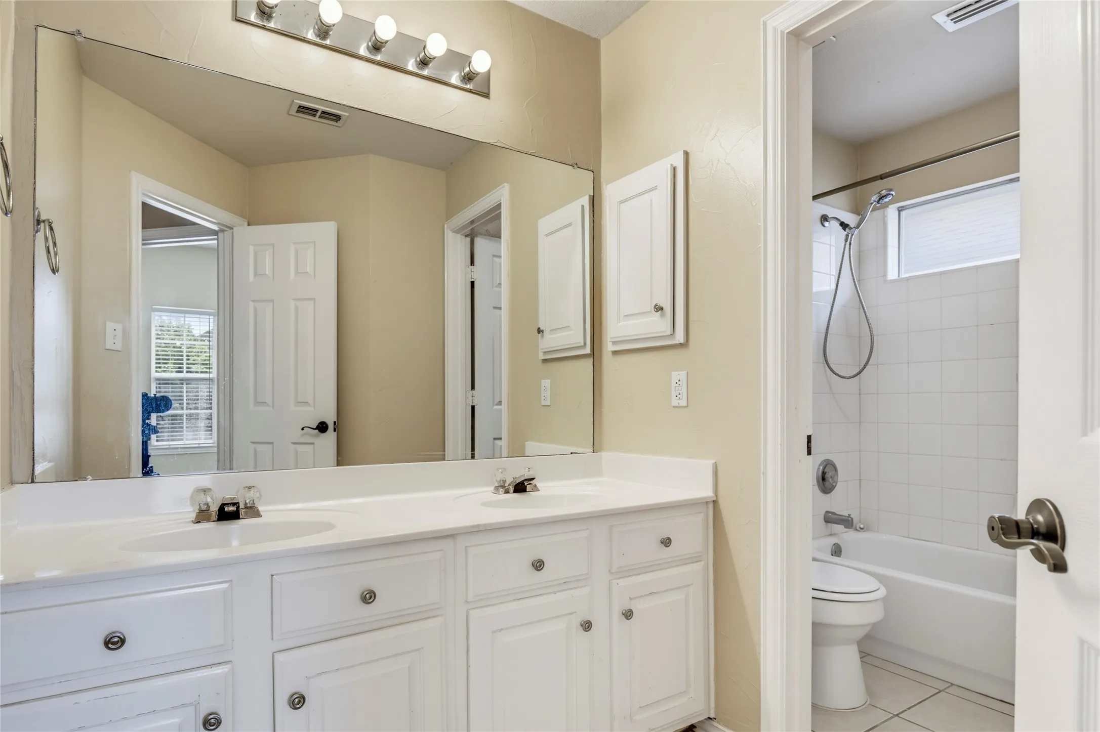 Dual vanity with white cabinetry, wall-mounted mirror, and overhead lighting