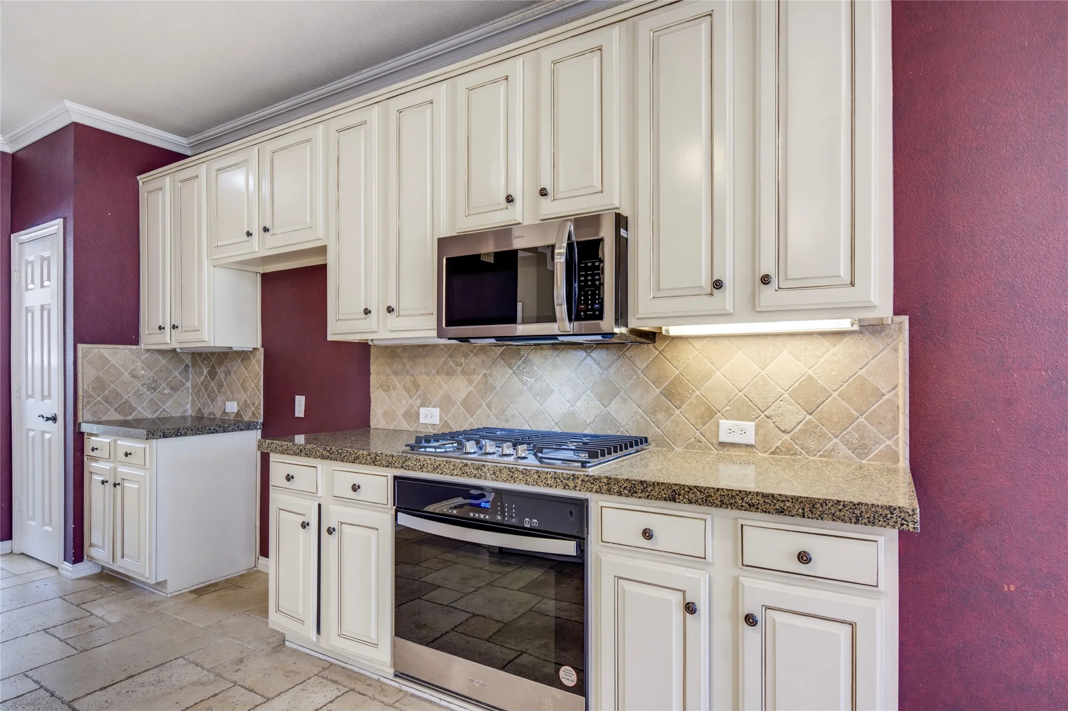 Kitchen featuring cream-painted cabinetry, stainless steel appliances, speckled countertops, and a tiled backsplash
