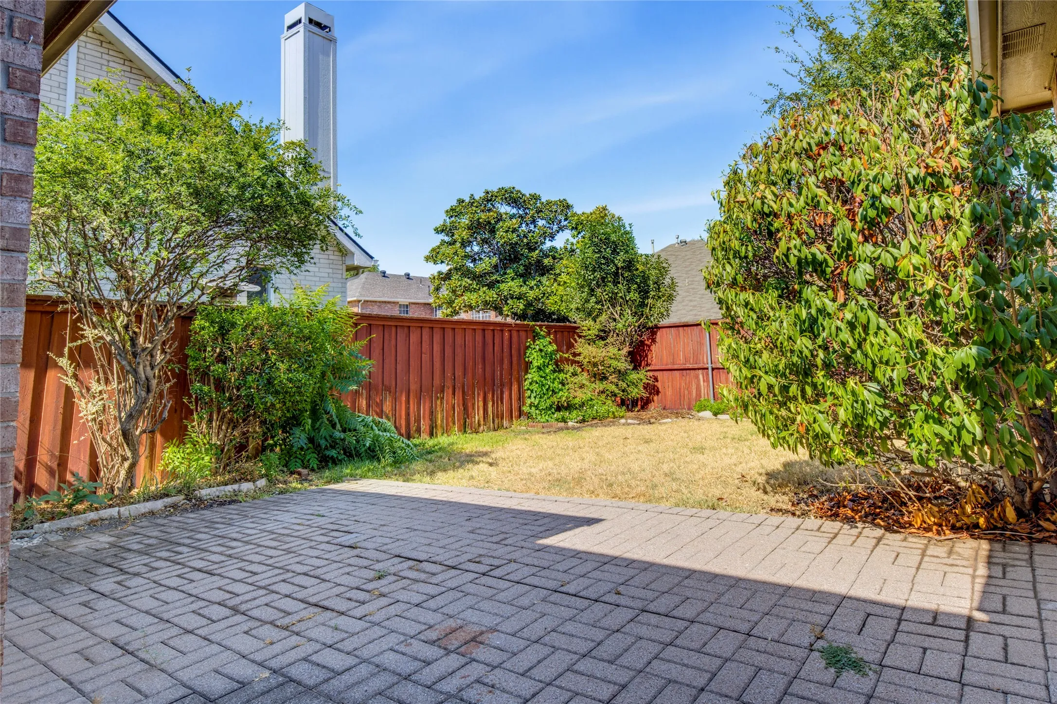 Paved patio area, fenced yard, mature landscaping, and an external chimney feature
