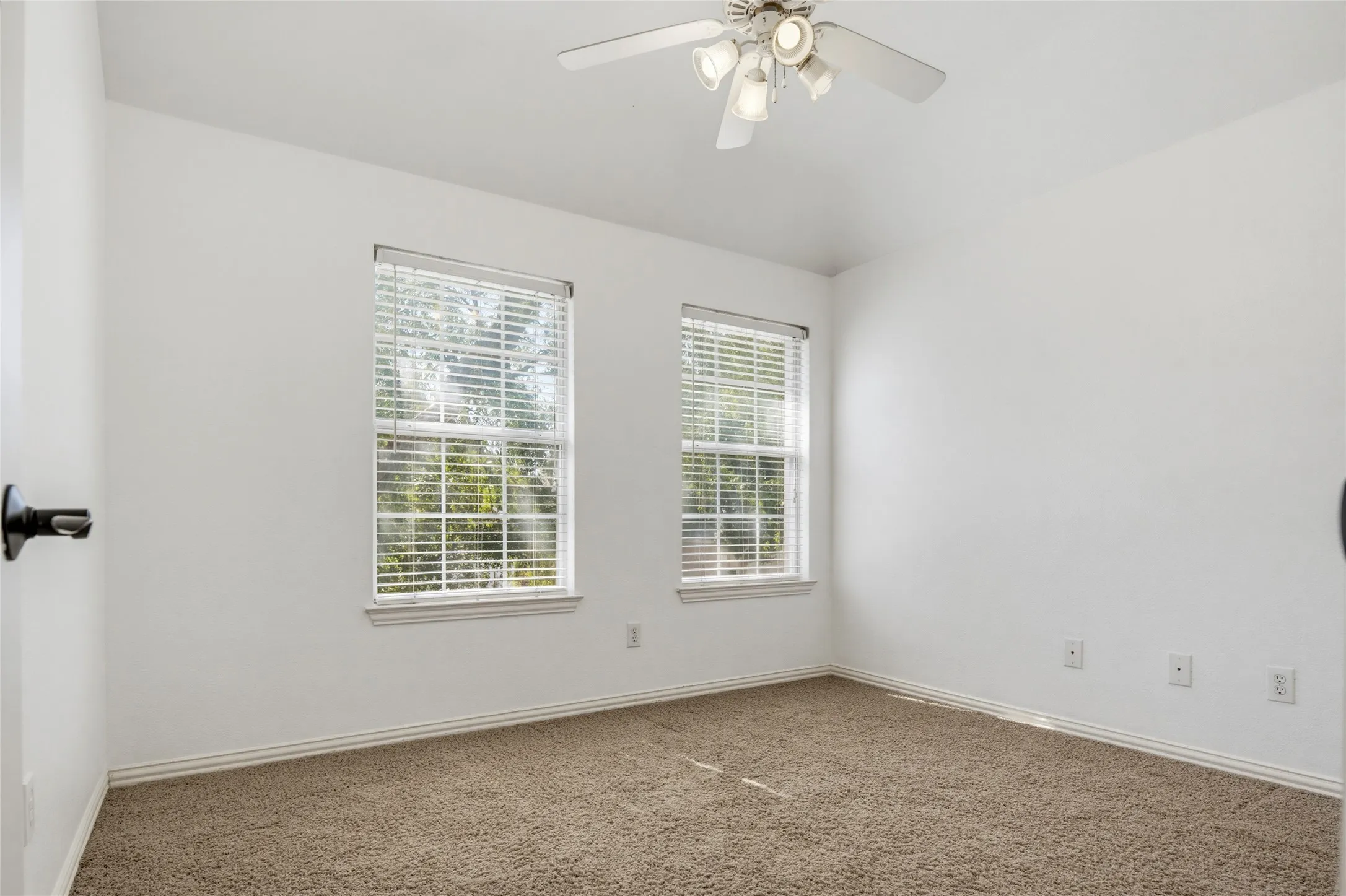 Neutral wall color, two windows with blinds, ceiling fan with integrated lighting, and carpeted flooring