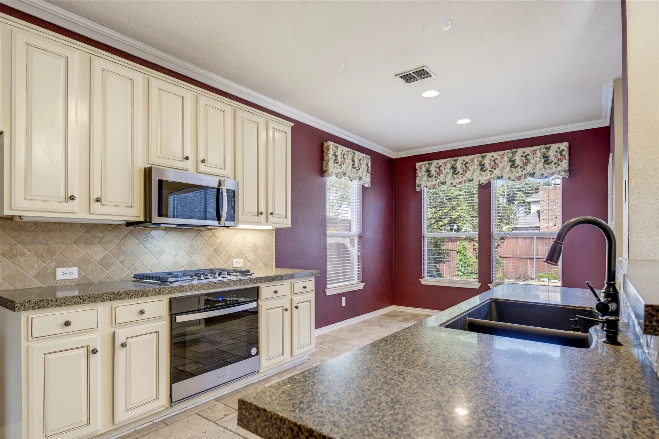 Kitchen featuring cream-painted cabinetry, stainless steel appliances, speckled countertops, a tile backsplash, and a large basin sink with a gooseneck faucet
